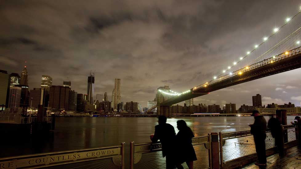 People stop along the Brooklyn waterfront to look at the dark Manhattan skyline. (AAP)
