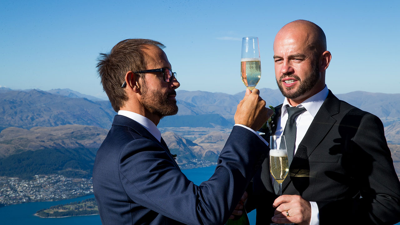 Having been delivered on the side of a mountain via helicopter, the grooms take some shots with champagne. 