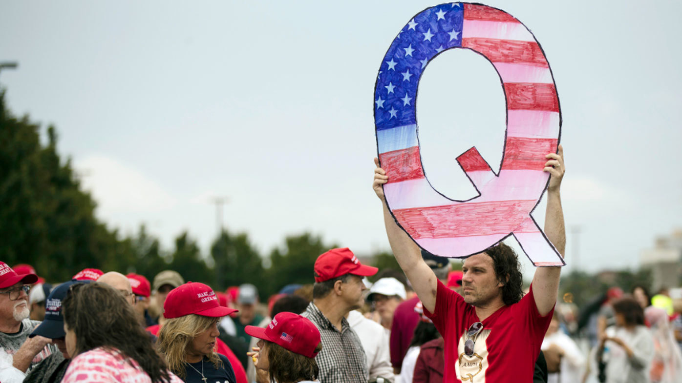 Un manifestante con un cartel Q espera con otros en un mitin de campaña realizado por el entonces presidente Donald Trump.