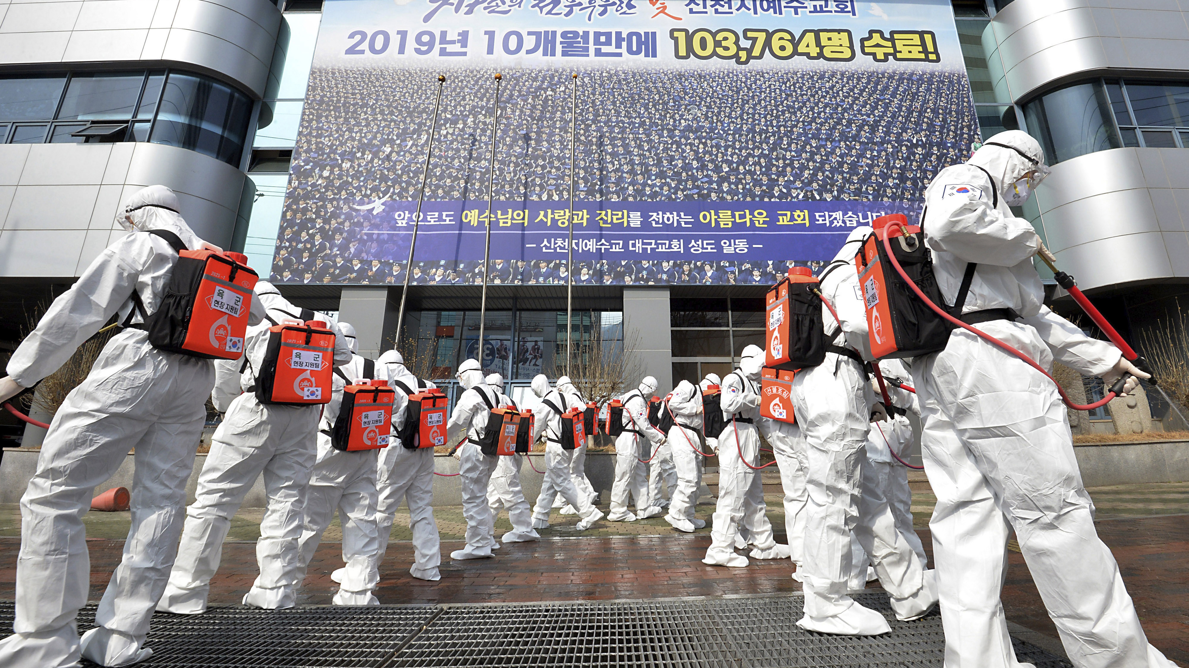 In this March 1, 2020, file photo, army soldiers wearing protective suits spray disinfectant to prevent the spread of the coronavirus in front of a branch of the Shincheonji Church of Jesus in Daegu, South Korea. As the coronavirus spreads around the world, many events that normally would draw large numbers of people are being canceled or played without fans. (Lee Moo-ryul/Newsis via AP, File)