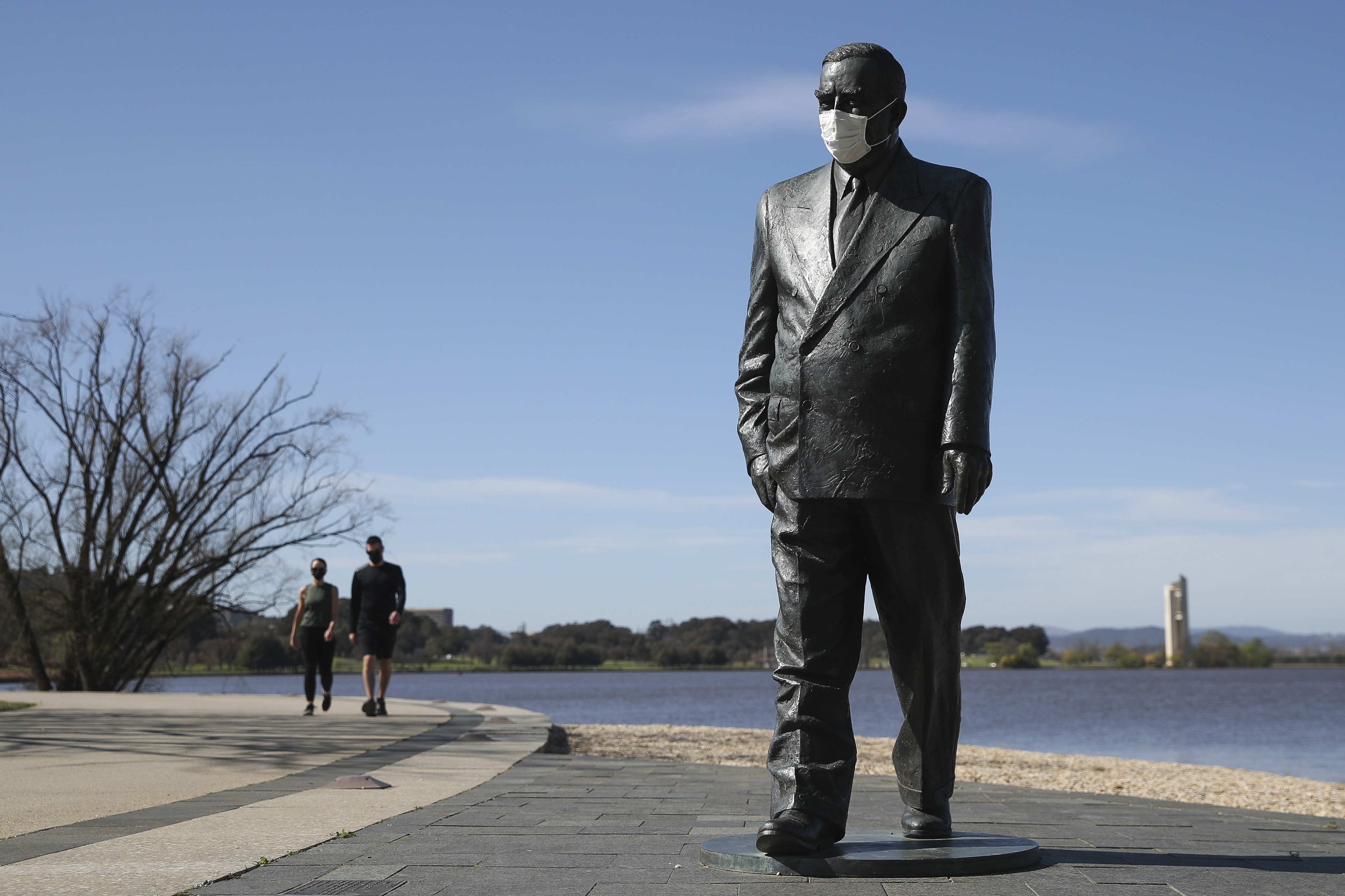A statue of former Prime Minister Sir Robert Menzies seen wearing a face mask, along Lake Burley Griffin in Canberra.