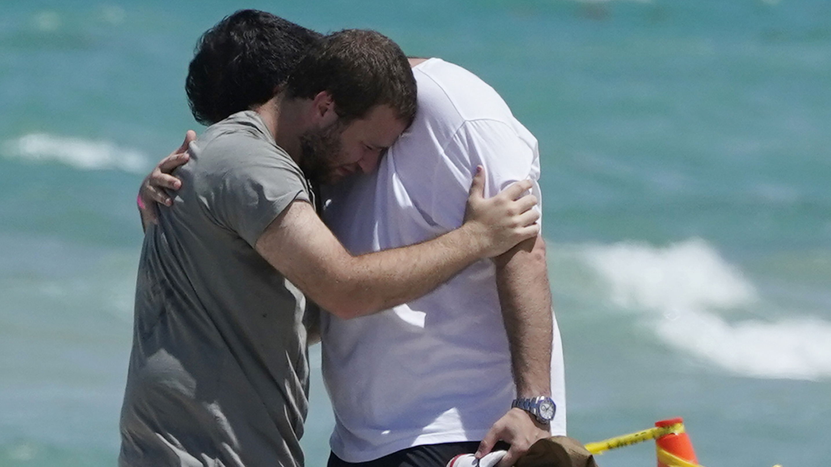 Two men console each other on the beach near the site of the Champlain Towers South condo tower in Florida.