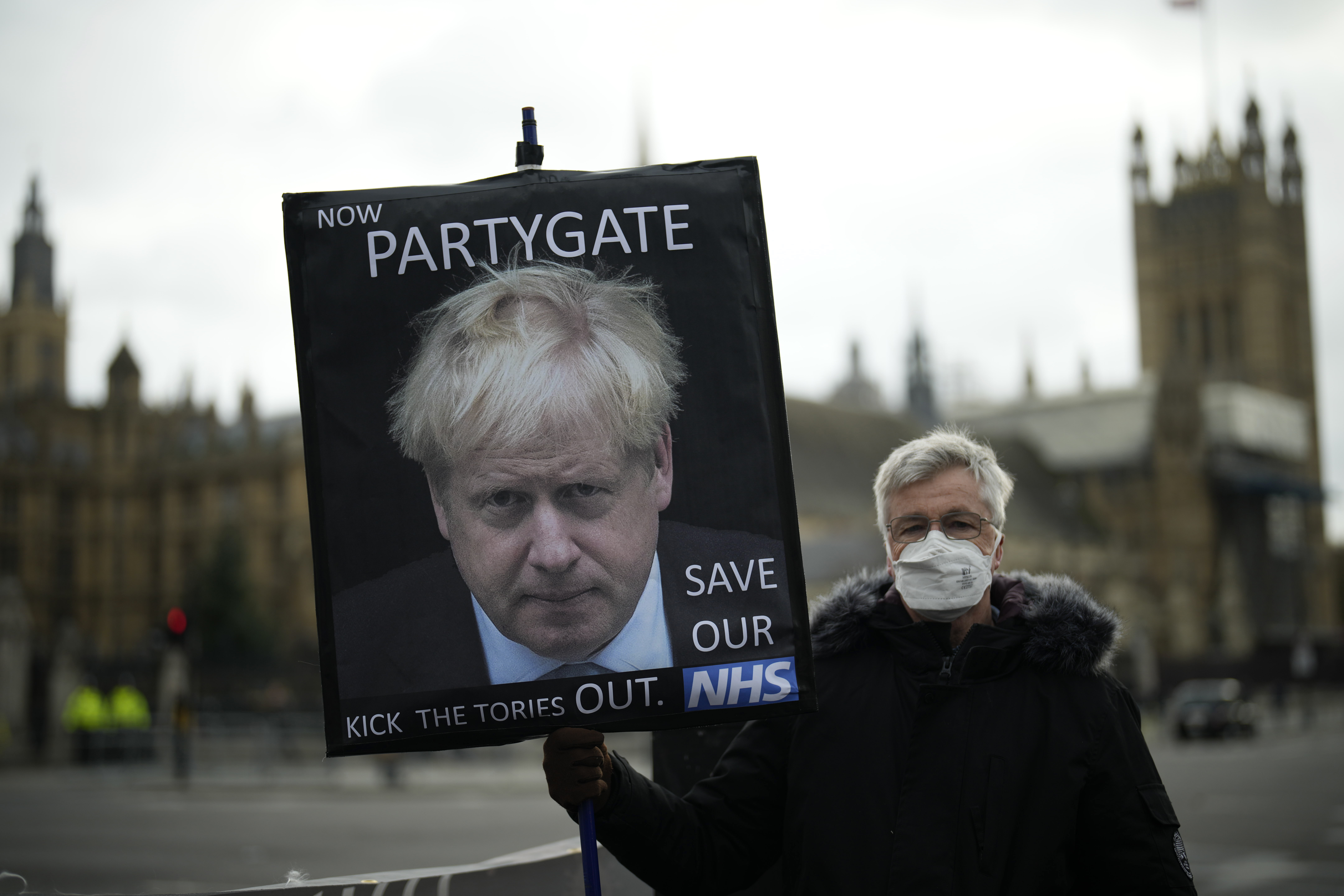 An anti-Conservative Party protester holds a placard with an image of British Prime Minister Boris Johnson including the words "Now Partygate" backdropped by the Houses of Parliament, in London. 