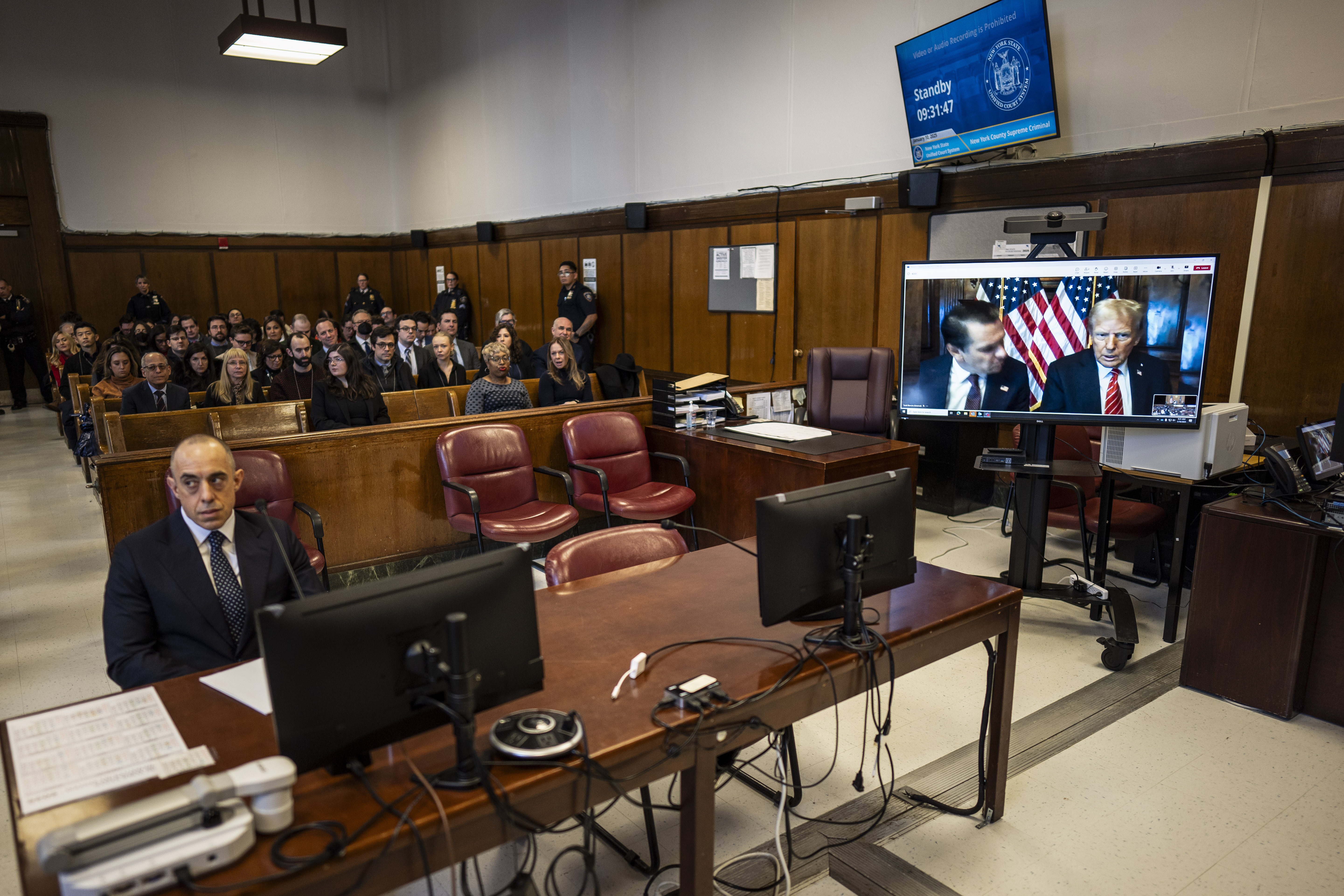 Attorney Emil Bove, left, listens as attorney Todd Blanche and President-elect Donald Trump, seen on a television screen