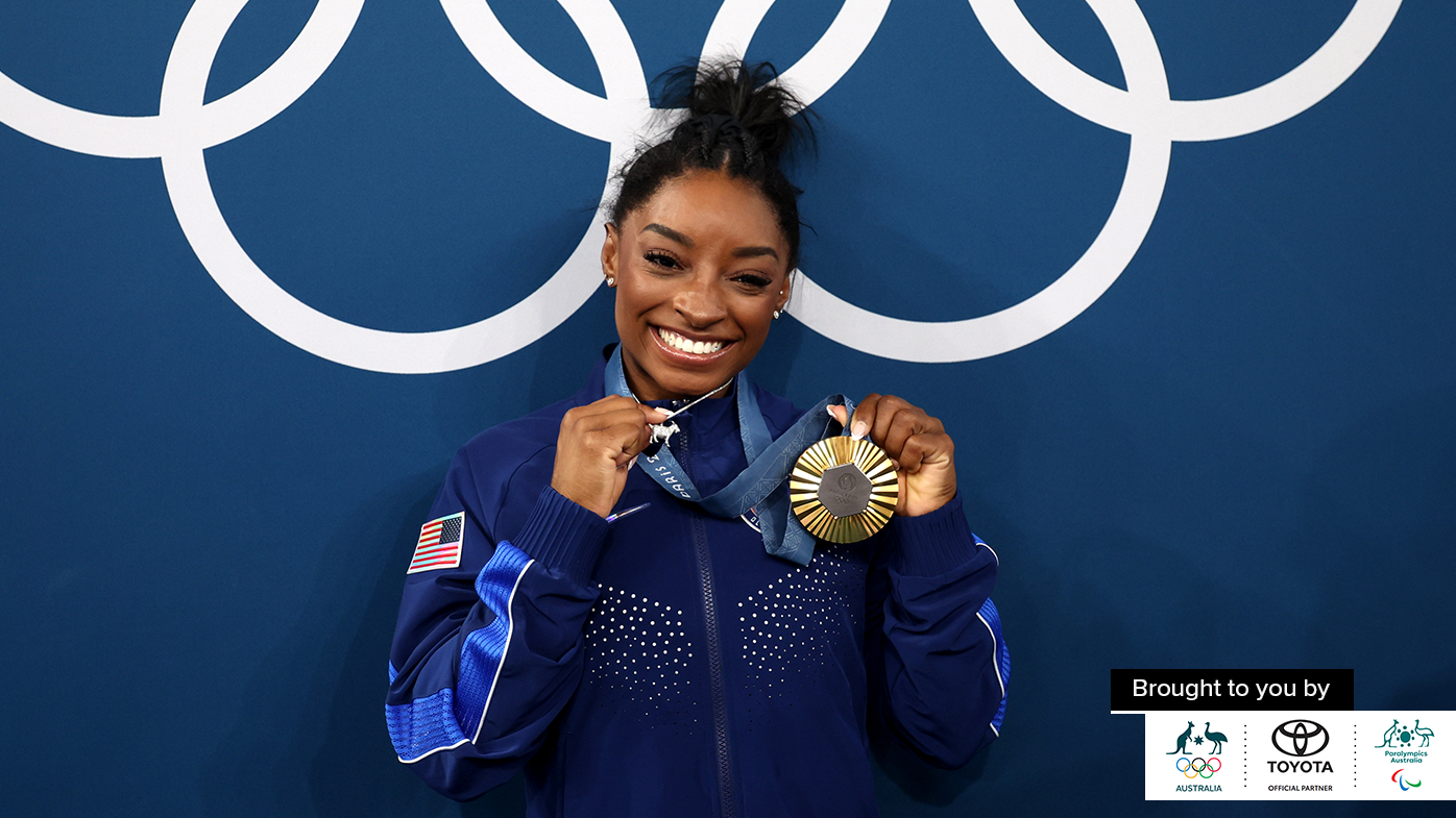 Simone Biles shows off a gold medal and a goat pendant.