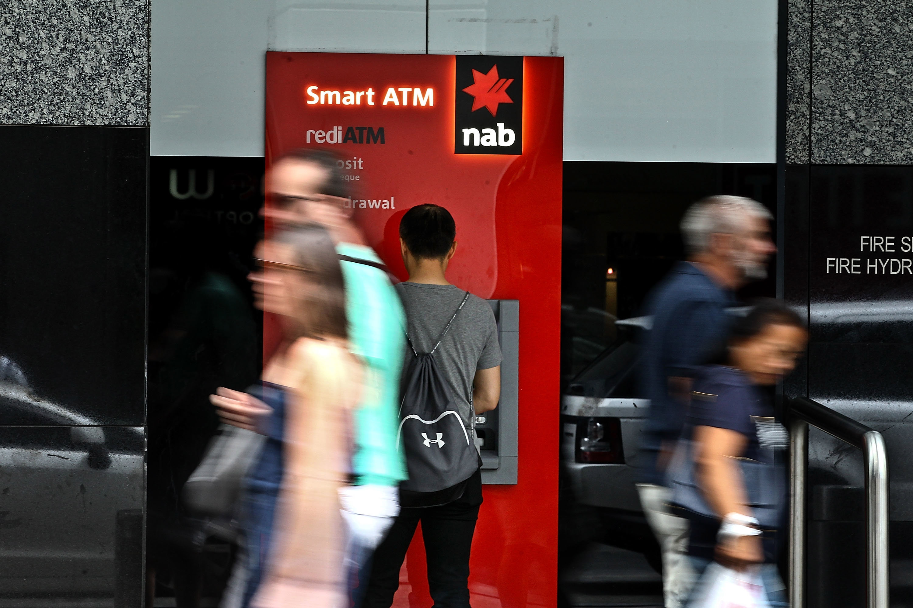A man uses an NAB ATM as pedestrians walk past.