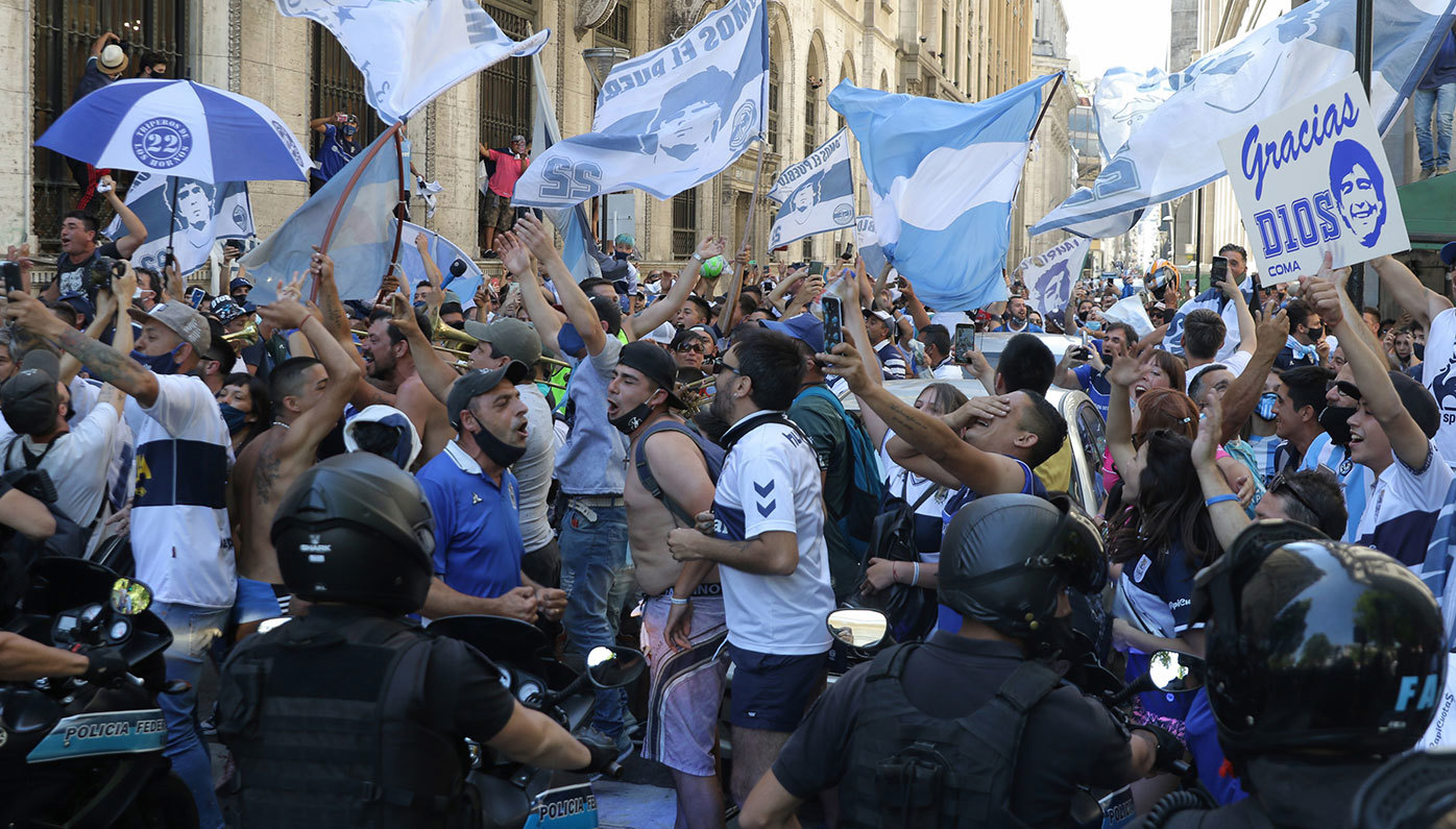 Fans sing and wave flags as the police tries to contain them during Diego Maradona's funeral in Buenos Aires, Argentina.