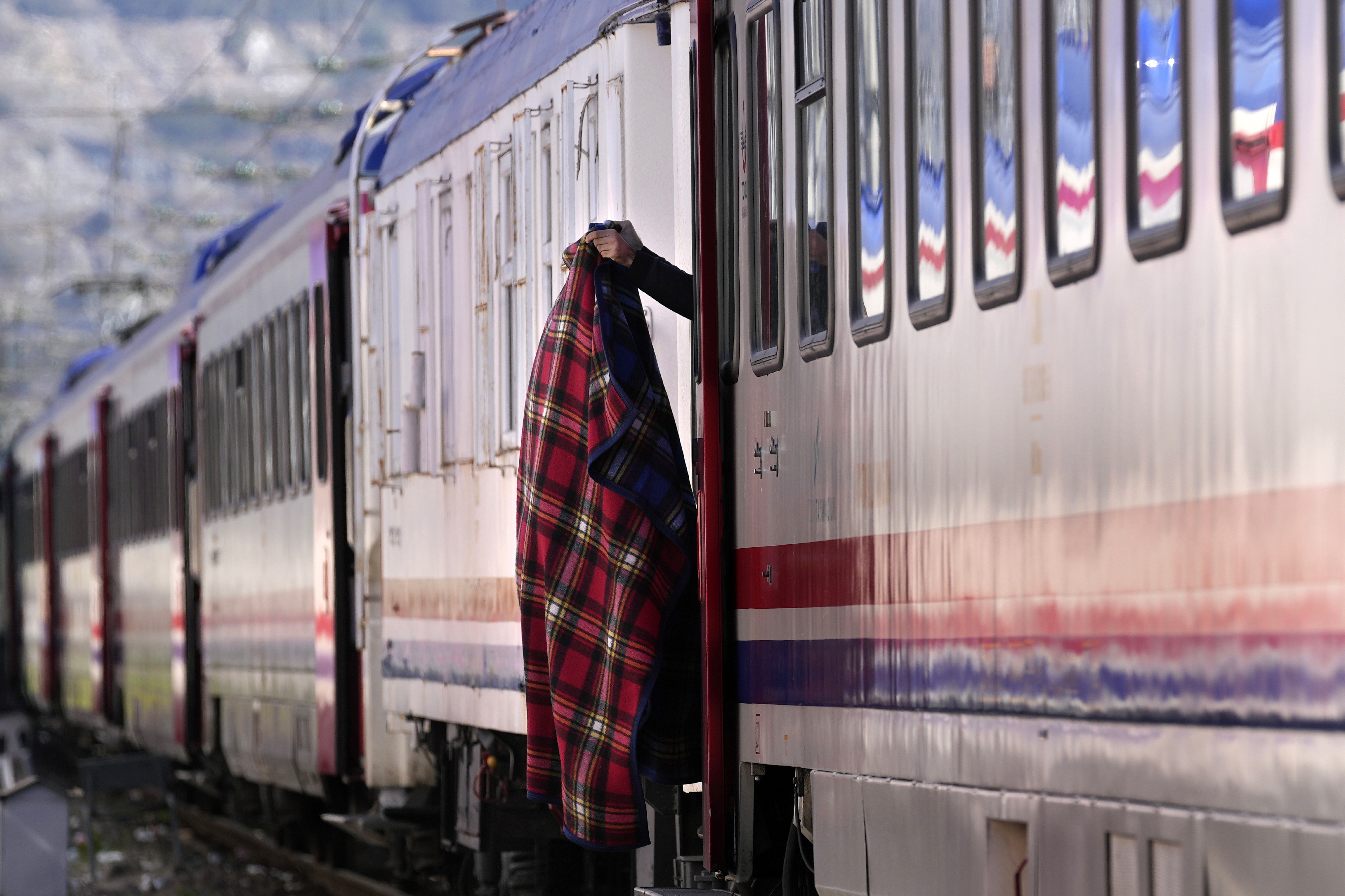 A man holds a blanket outside a train using as a shelter in Iskenderun city, southern Turkey, Tuesday, Feb. 14, 2023. 