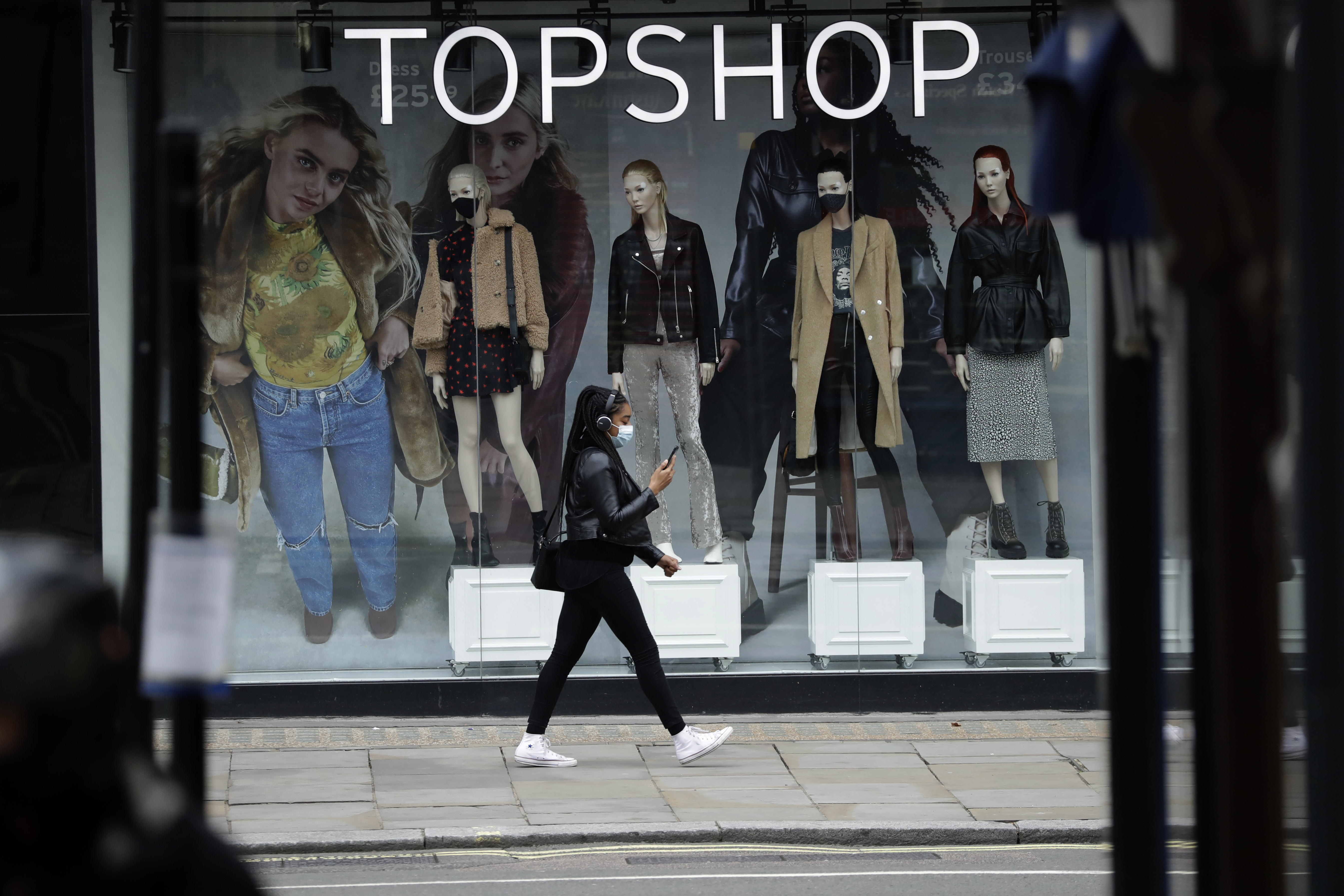 A woman wearing a face mask walks past mannequins wearing face masks in the window of a temporarily closed branch of the Topshop women's clothing chain during England's second coronavirus lockdown, in London.