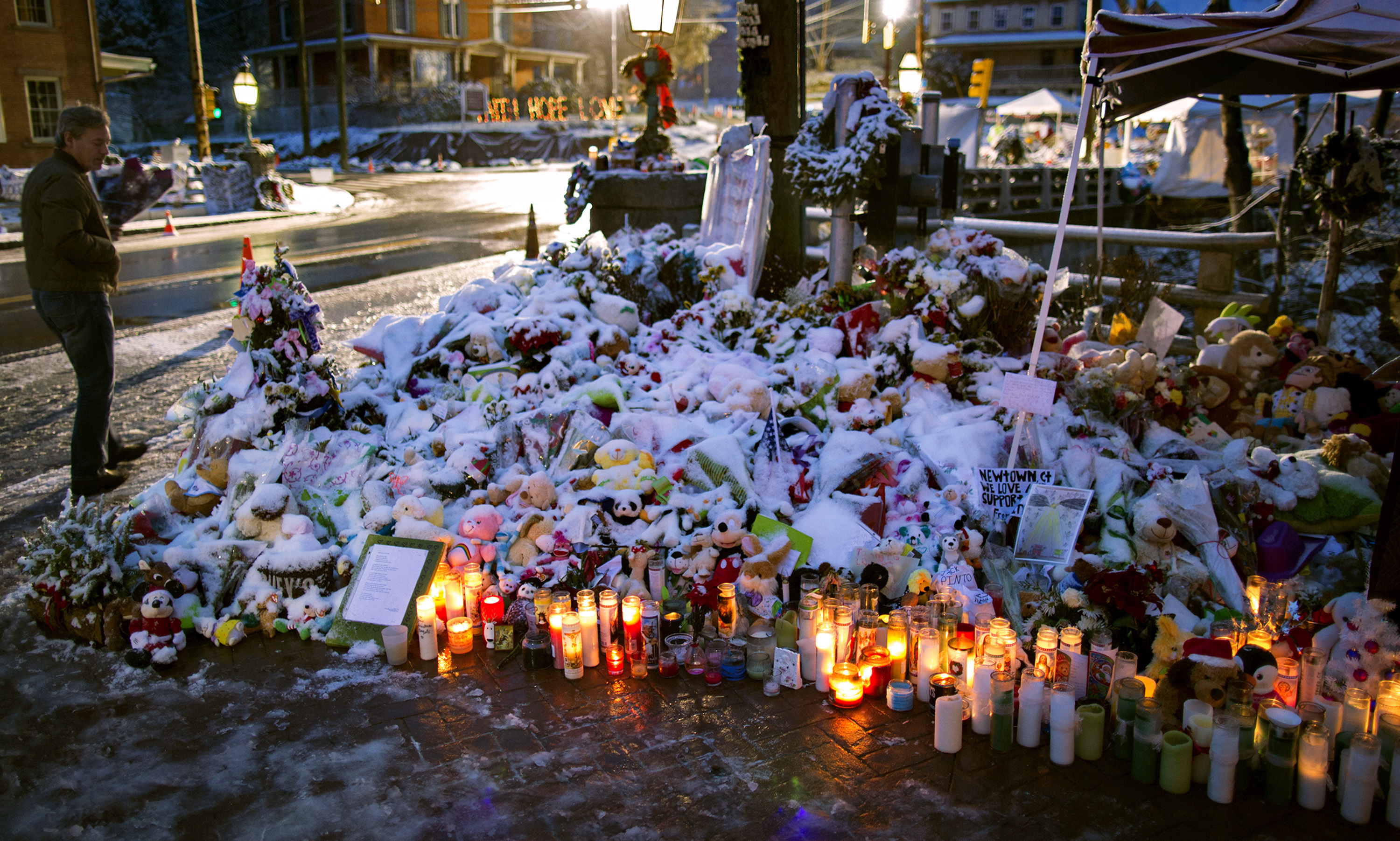 ARCHIVO - En esta fotografía de archivo del 25 de diciembre de 2012, un miembro de la familia Rutter de Sandy Hook, Connecticut, camina junto a velas y otras ofrendas que conforman un monumento a las víctimas del tiroteo en la escuela primaria Sandy Hook en Newtown, Connecticut. Después de casi ocho años de discusión y planificación, se está a punto de construir un monumento permanente a las víctimas con el objetivo de ofrecer un lugar pacífico para la reflexión. (Foto AP/Craig Ruttle, archivo)