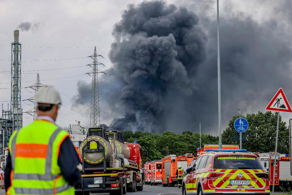 Emergency vehicles of the fire brigade, rescue services and police stand not far from an access road to the Chempark over which a dark cloud of smoke is rising in Leverkusen, Germany, Tuesday, July 27, 2021