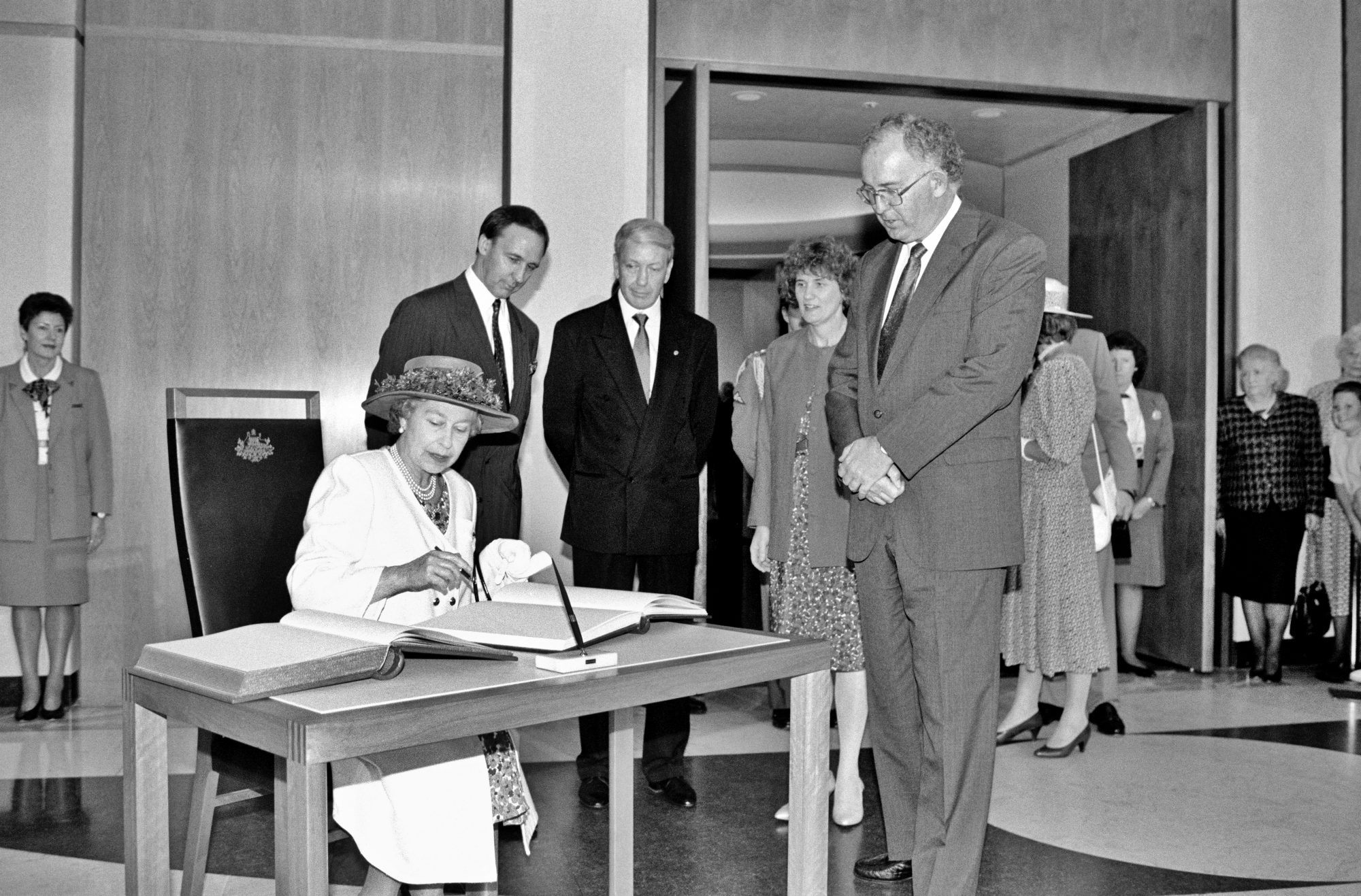 Her Royal Highness Queen Elizabeth II signs the visitors' book at Parliament House, while Prime Minister Paul Keating and Parliament House officials look on, February 1992.