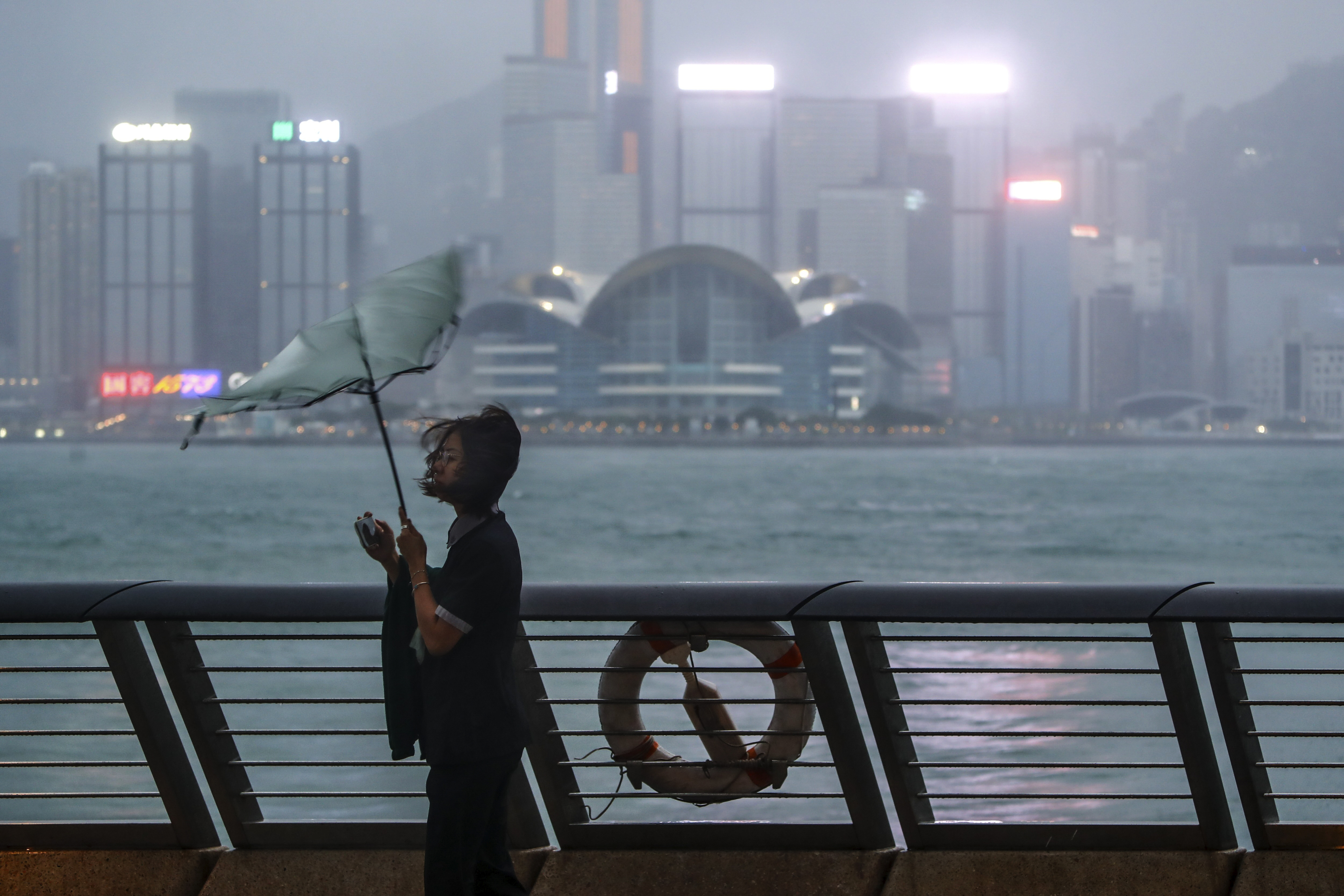 A woman's umbrella is blown at the seaside as typhoon Saola strikes the city with strong winds and rain, in Hong Kong, Friday, Sept. 1, 2023. 