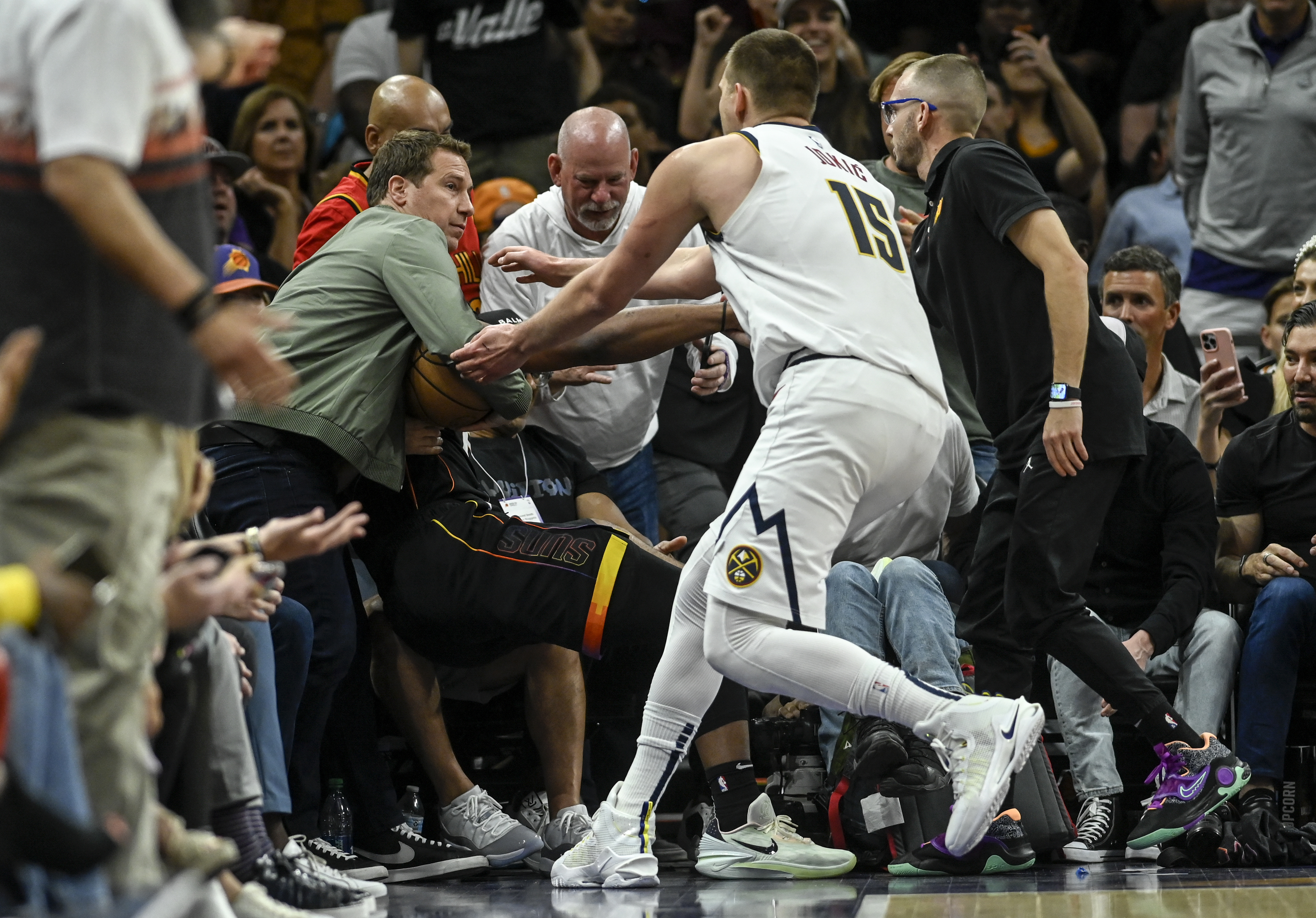 PHOENIX, AZ - MAY 7: Nikola Jokic (15) of the Denver Nuggets rushes to retrieve the game ball as Phoenix Suns owner Mat Ishbia inserts himself into the action by clutching the ball as he helps Josh Okogie (2) to his feet after Okogie flew into the stands during the second quarter at Footprint Center in Phoenix on Sunday, May 7, 2023. (Photo by AAron Ontiveroz/The Denver Post)
