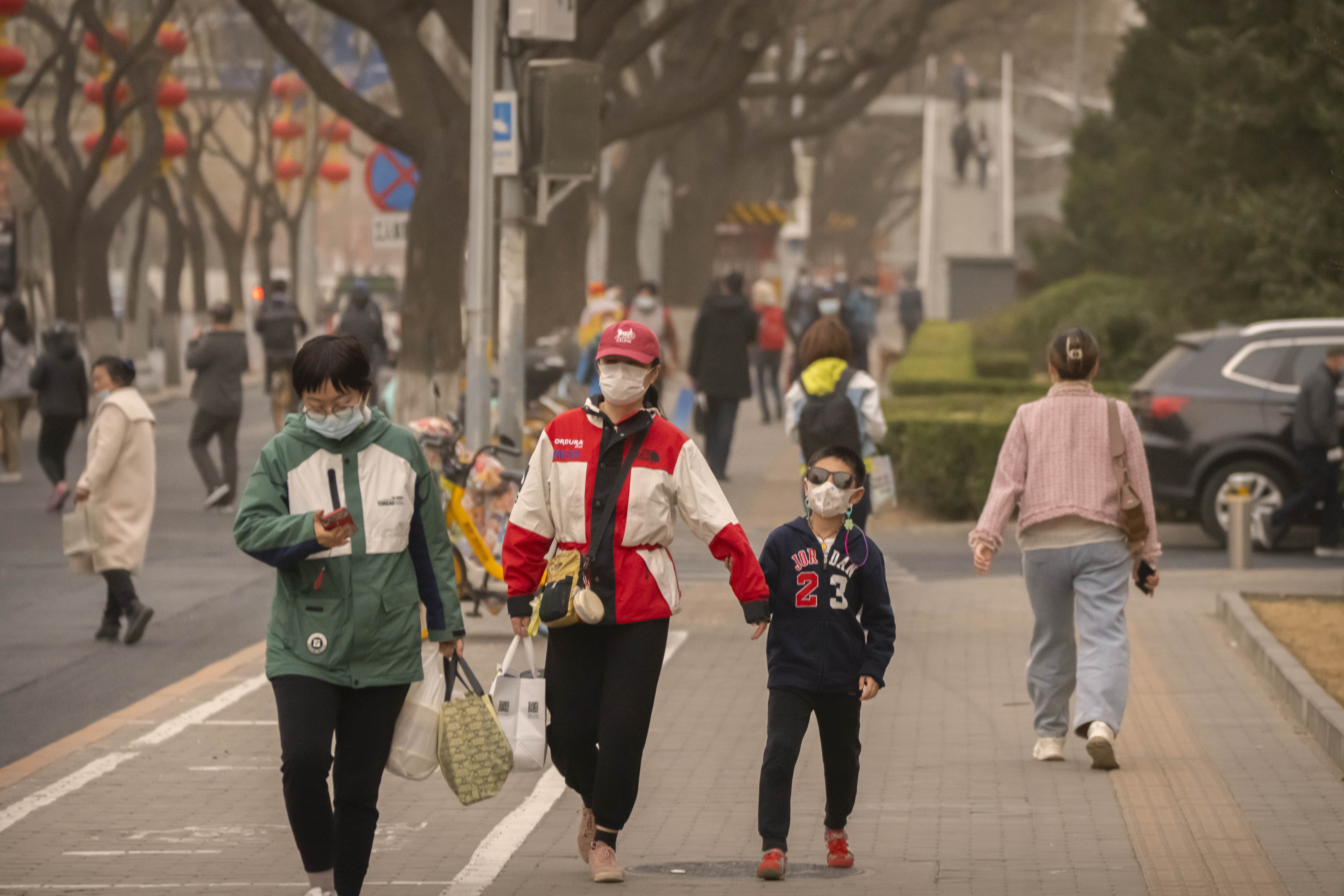 People wearing face masks walk along a street during a day with poor air quality in Beijing, Friday, March 10, 2023.