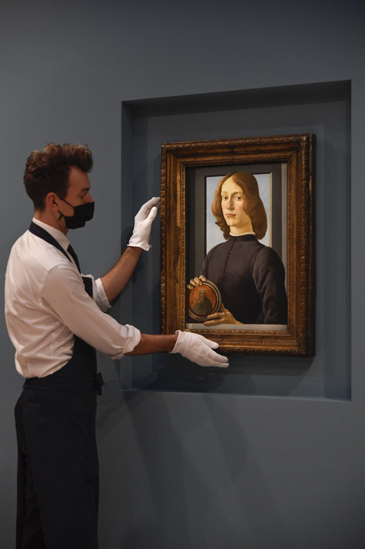 A member of the staff wearing a face mask to curb the spread of COVID-19 holds the painting 'Young Man Holding a Roundel' by the Italian Renaissance painter Sandro Botticelli at Sotheby's, in London, Wednesday, Dec. 2, 2020. 
