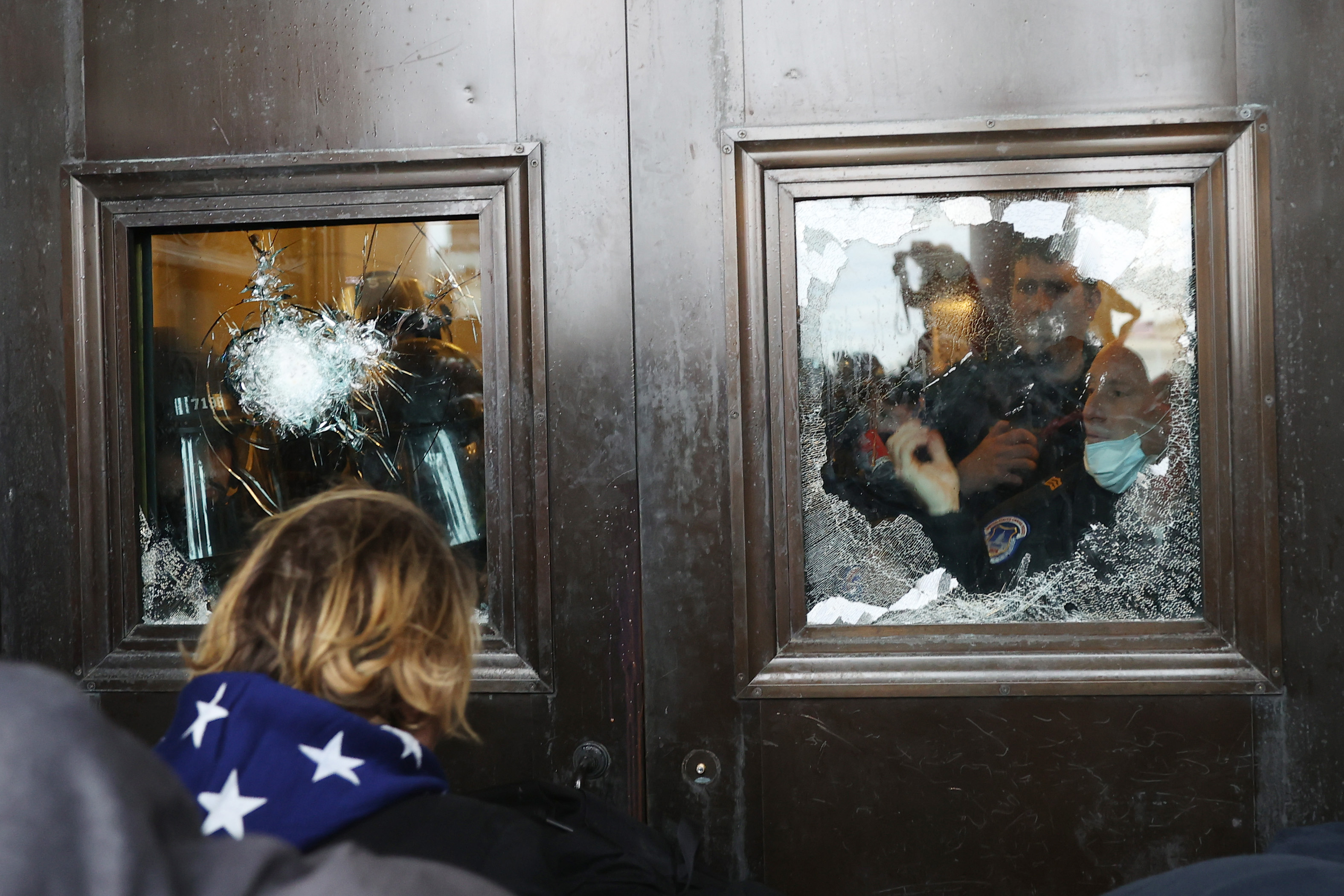 A Capitol police officer looks out of a broken window as protesters gather on the US Capitol Building 