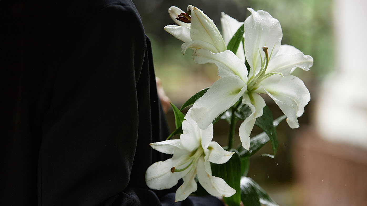 Close up on white lilies in hands of unrecognizable person wearing black suit while raindrops gently dripping on delicate petals, copy space