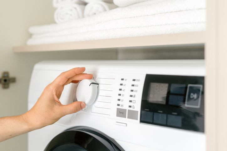Woman choose delicate dryer settings and stars laundry at home, close up. Female hand turn knob, adjust program at modern washing machine in a well designed room. Household appliance in modern house