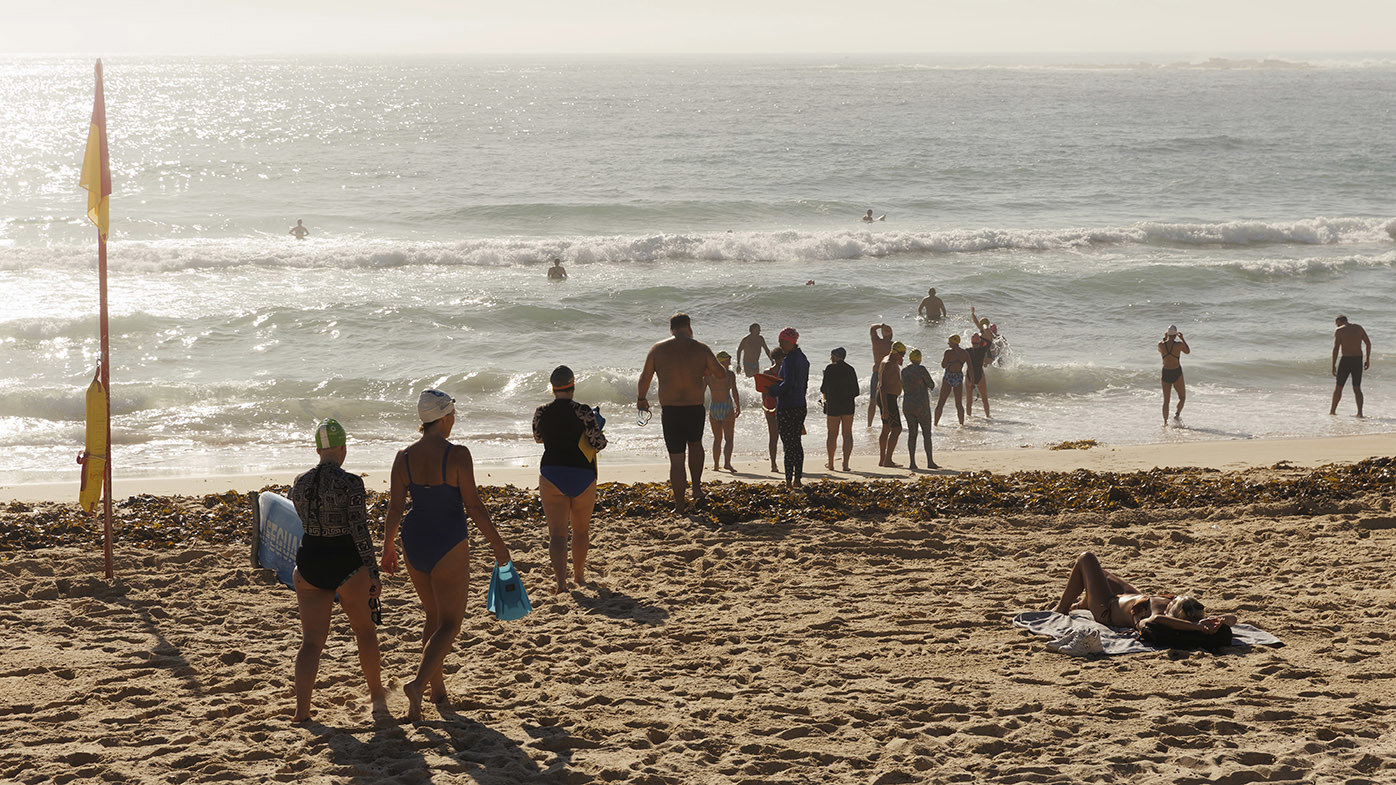 Ocean swimmers head into the water at Coogee in Sydney as the sun shines on the water.