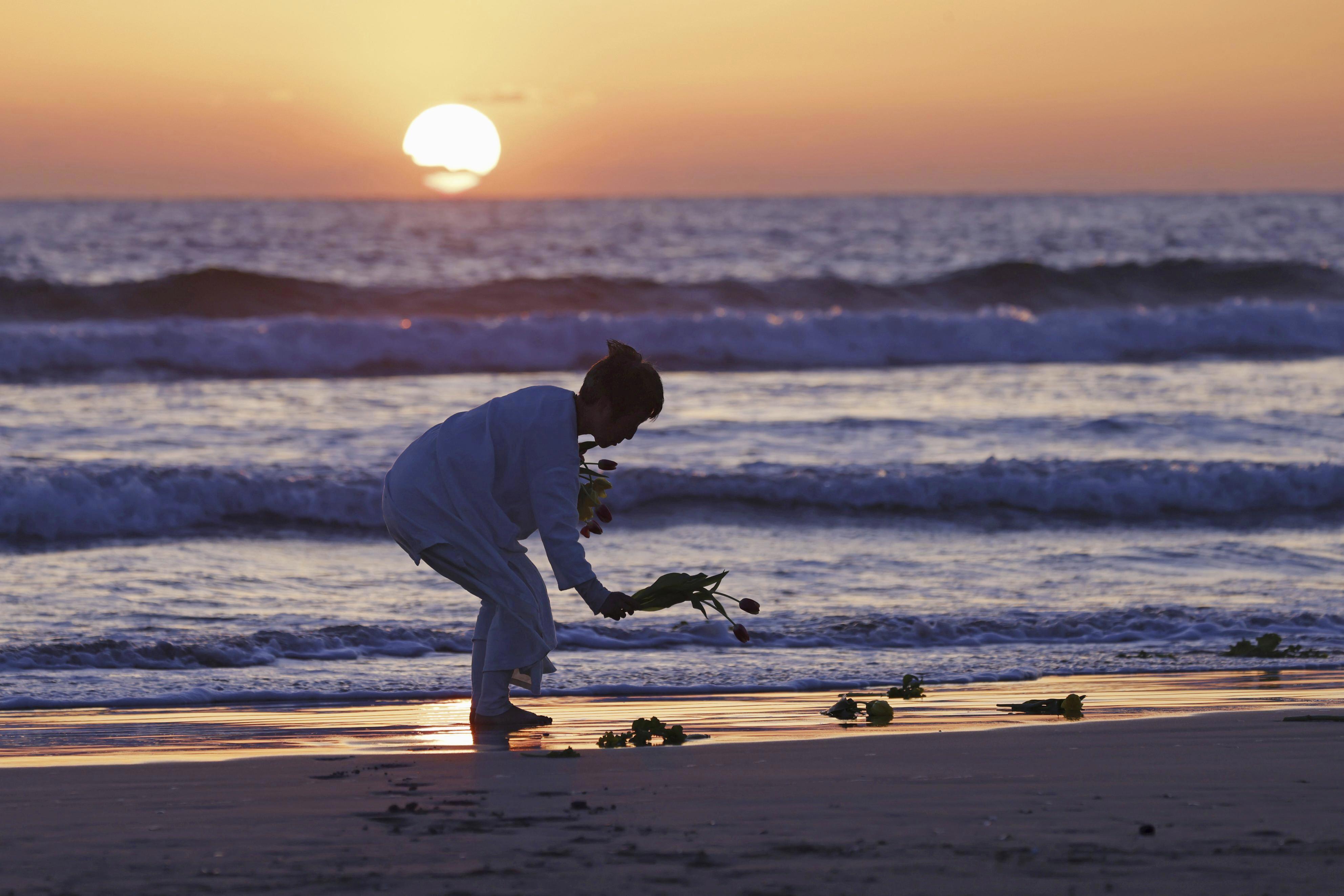 A woman places flowers on beach in Iwaki city, Fukushima prefecture on Saturday, March 11, 2023. 