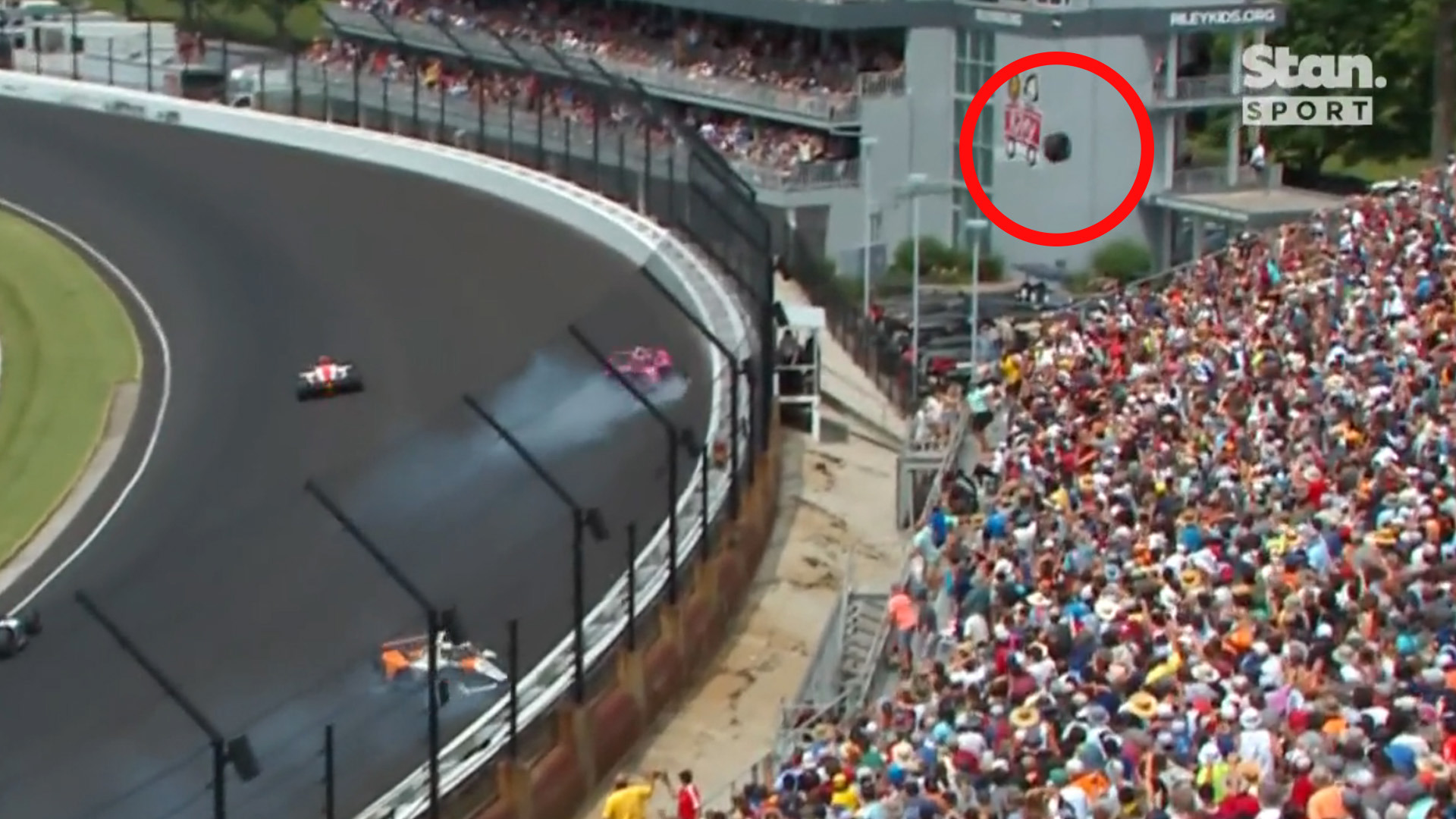 A wheel from Kyle Krikwood's car flies out of the confines of the race track, narrowly avoiding the packed grandstand.
