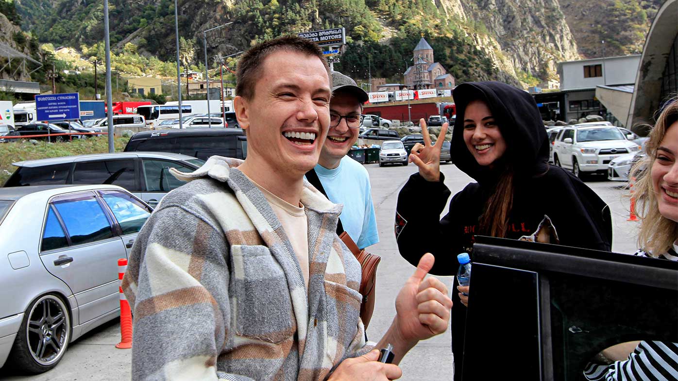 Young Russians grinning at the camera after crossing the border into Georgia rather than be drafted into the military.