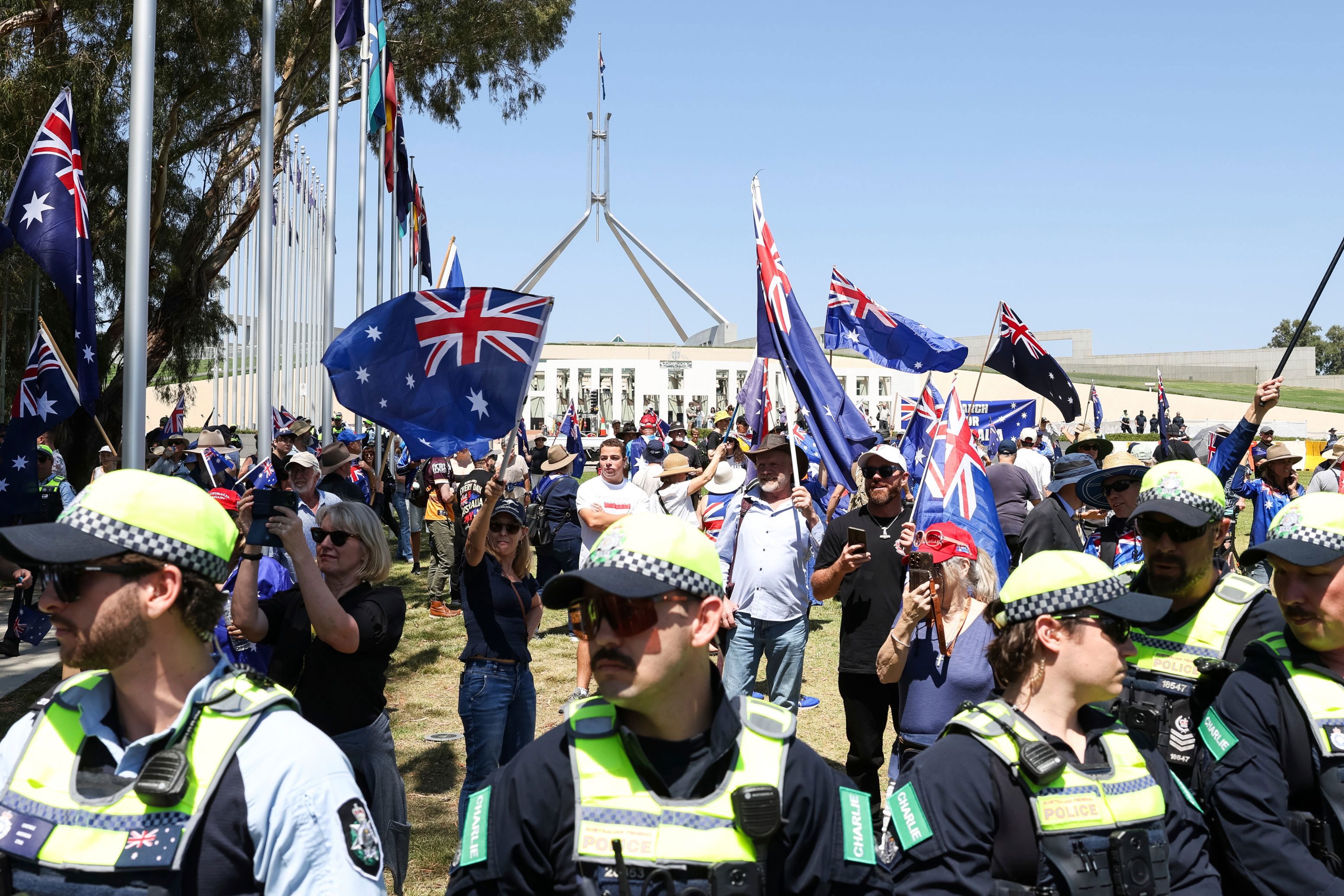 People from the March for Australia rally (in the background) at the front of Parliament House in Canberra on Monday 26 January 2026. fedpol Photo: Alex Ellinghausen