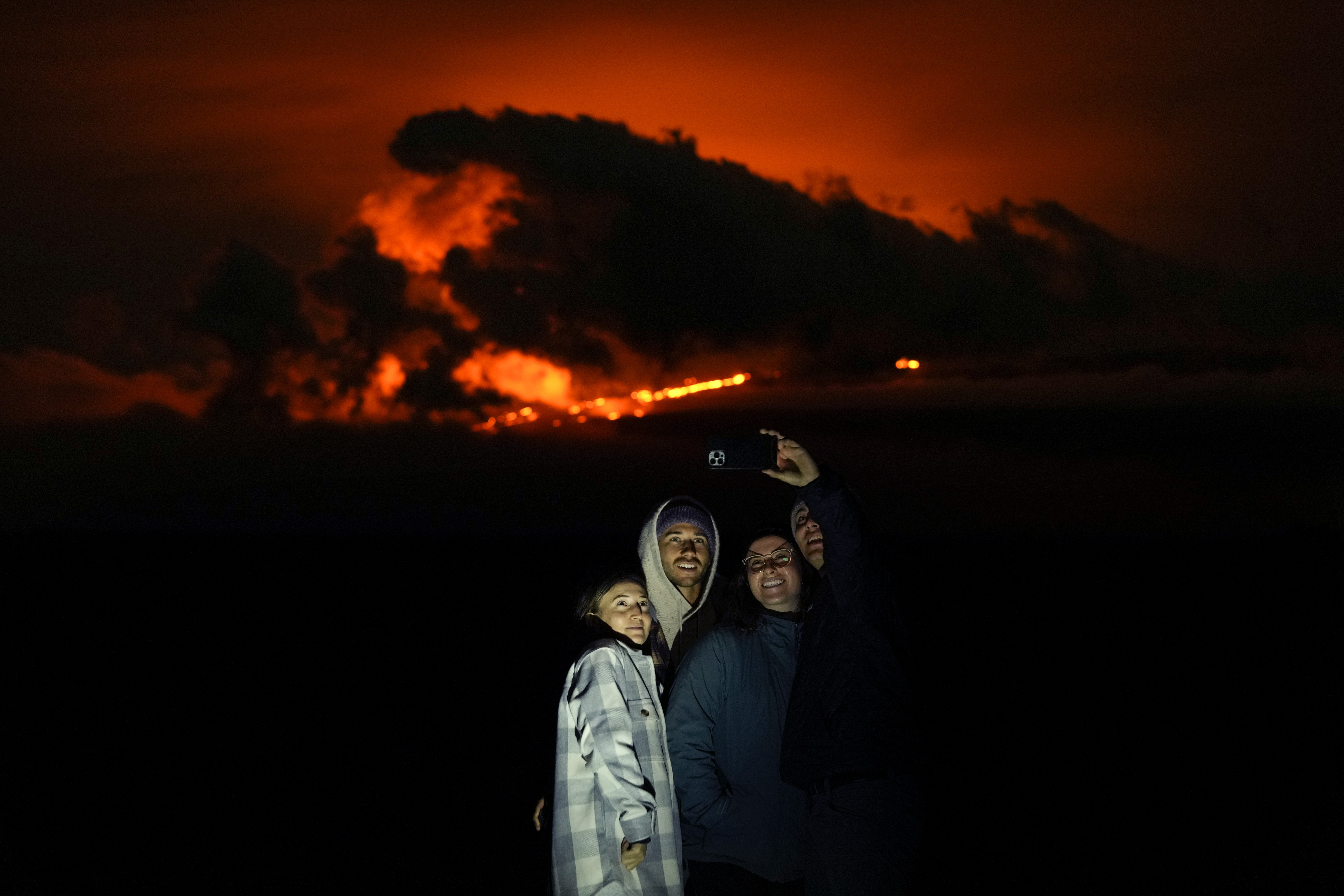 Ashlyn Nadeau, a la izquierda, junto a su esposo, Casey Nadeau, segundo desde la izquierda;  Jessica Doyle, segunda desde la derecha, y Justin Potter, a la derecha, mientras toman una foto debajo del volcán Mauna Loa en erupción el viernes 2 de diciembre de 2022, cerca de Hilo, Hawái.