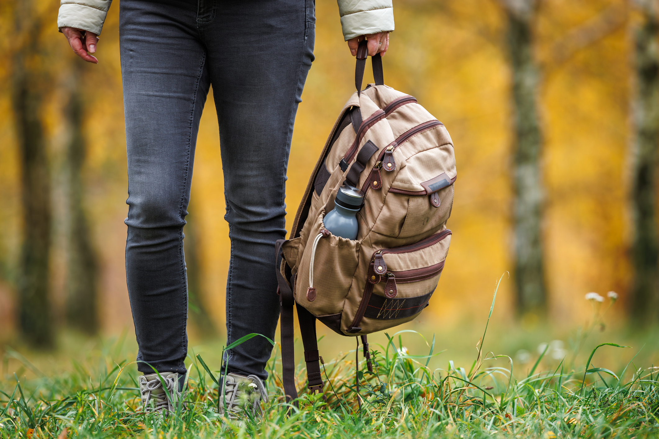 Female hiker holding backpack in hand. Woman trekking in autumn forest. Adventure in nature