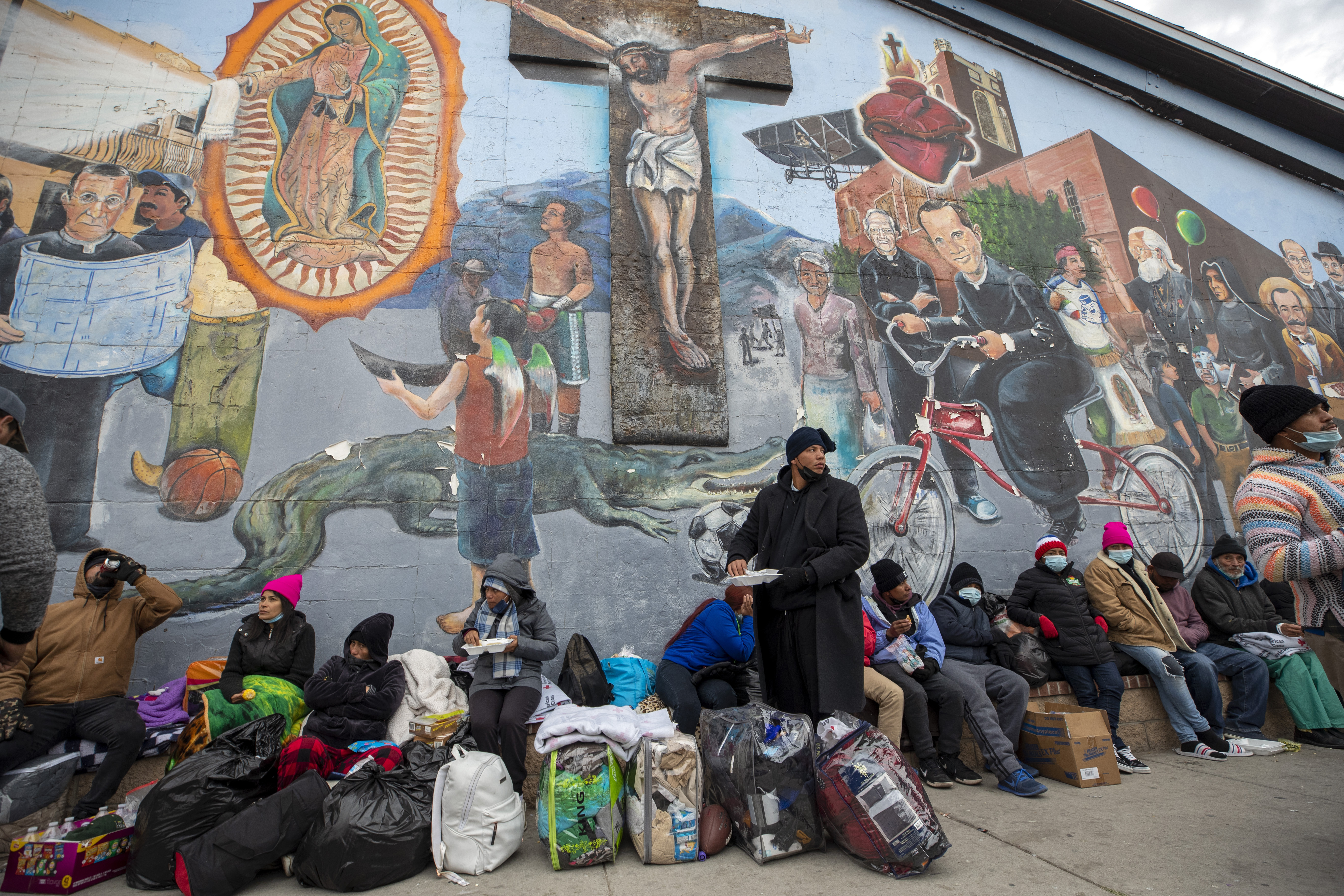 Migrantes comen y esperan ayuda mientras acampan en una calle del centro de El Paso, Texas, el domingo 18 de diciembre de 2022. Las ciudades fronterizas de Texas se preparaban el domingo para una oleada de hasta 5,000 nuevos migrantes por día en la frontera entre Estados Unidos y México. ya que las restricciones de inmigración de la era de la pandemia expiran esta semana, poniendo en marcha planes para proporcionar vivienda de emergencia, alimentos y otros elementos esenciales.  (Foto AP/Andrés Leighton)