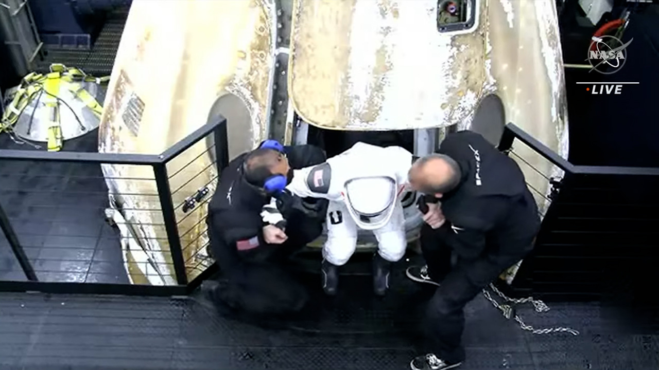 A member of the SpaceX crew is helped out of the Dragon capsule after returning from the International Space Station.