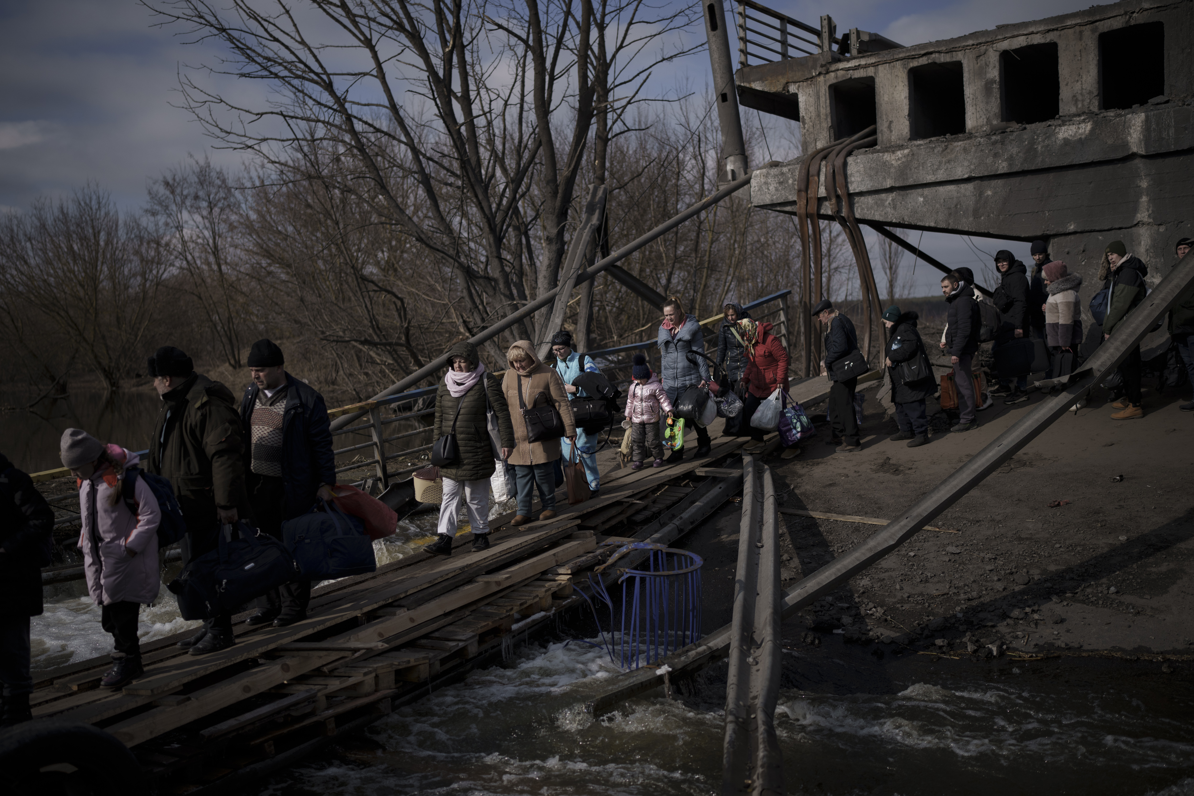Ukrainians cross an improvised path under a destroyed bridge while fleeing Irpin, on the outskirts of Kyiv, Ukraine, Wednesday, March 9, 2022 