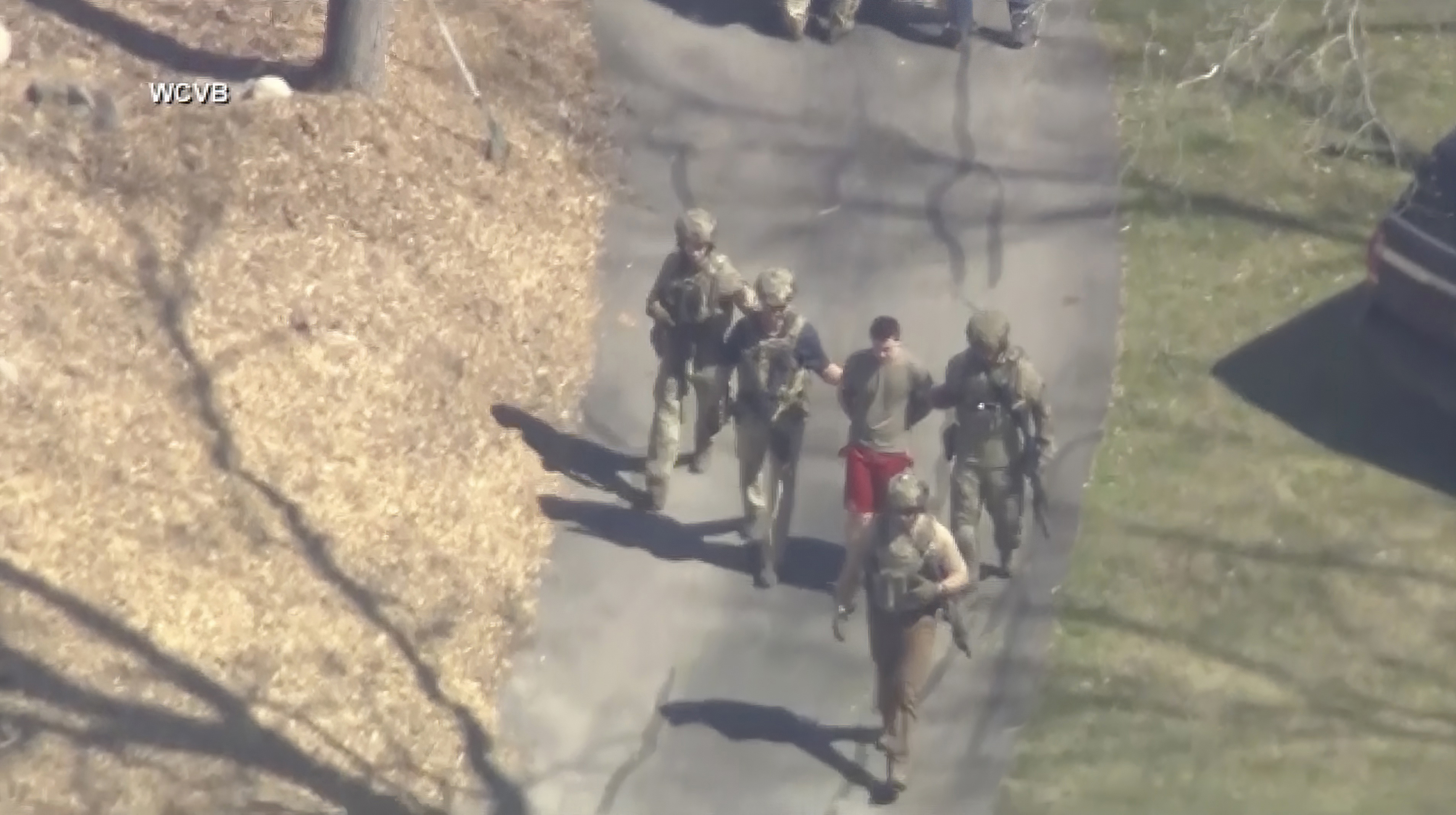 Esta imagen tomada de un video proporcionado por WCVB-TV muestra a Jack Teixeira, en camiseta y pantalones cortos, siendo detenido por agentes tácticos armados el jueves 13 de abril de 2023 en Dighton, Massachusetts. 