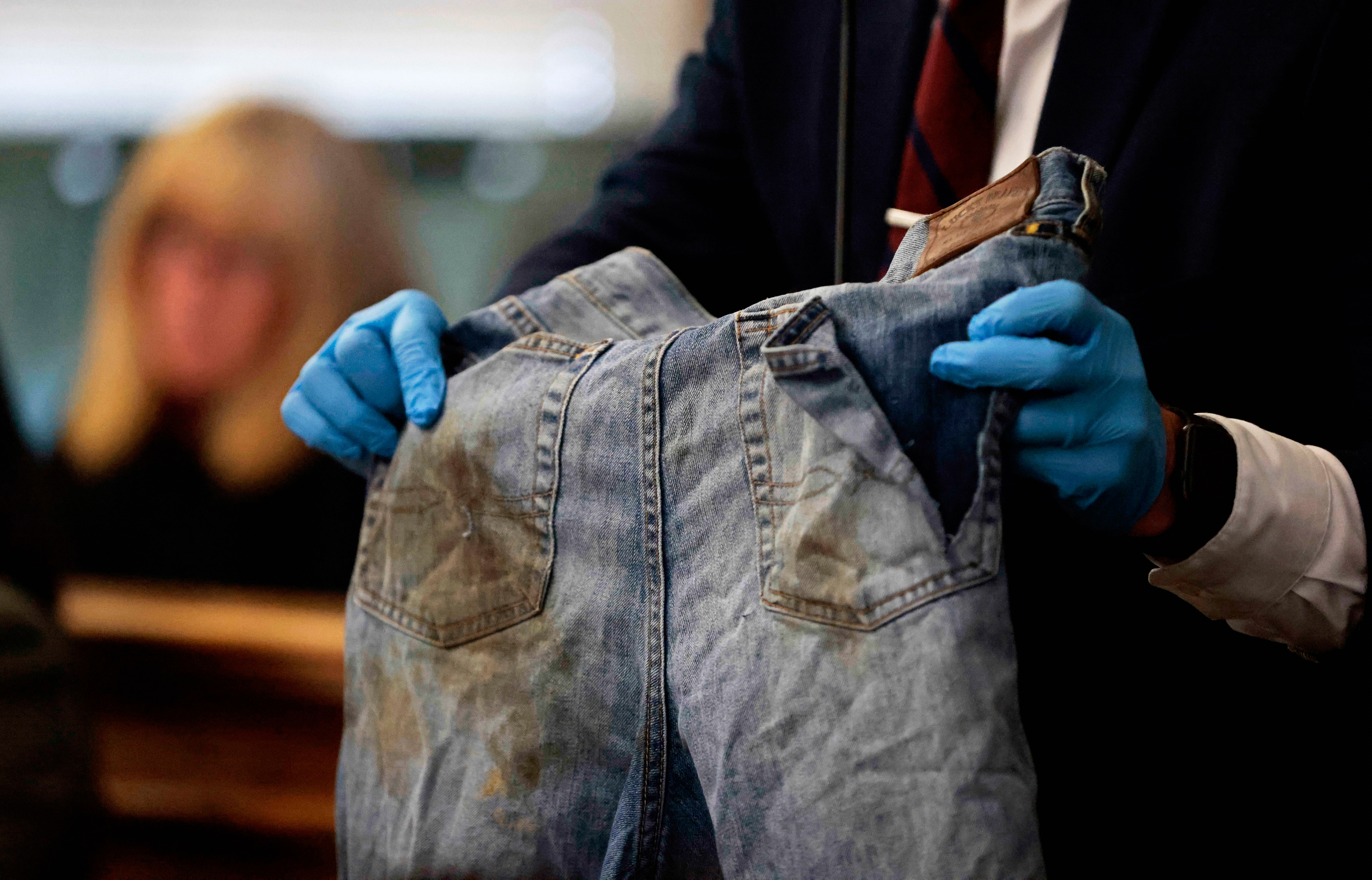 Sgt. Yuriy Bukhenik, of the Massachusetts State Police, holds the stained jeans cut from Boston Police officer John O'Keefe as he returns to the witness stand in the murder retrial of Karen Read in Norfolk Superior Court, Monday, May 12, 2025, in Dedham, Mass. (Pat Greenhouse/The Boston Globe via AP, Pool)