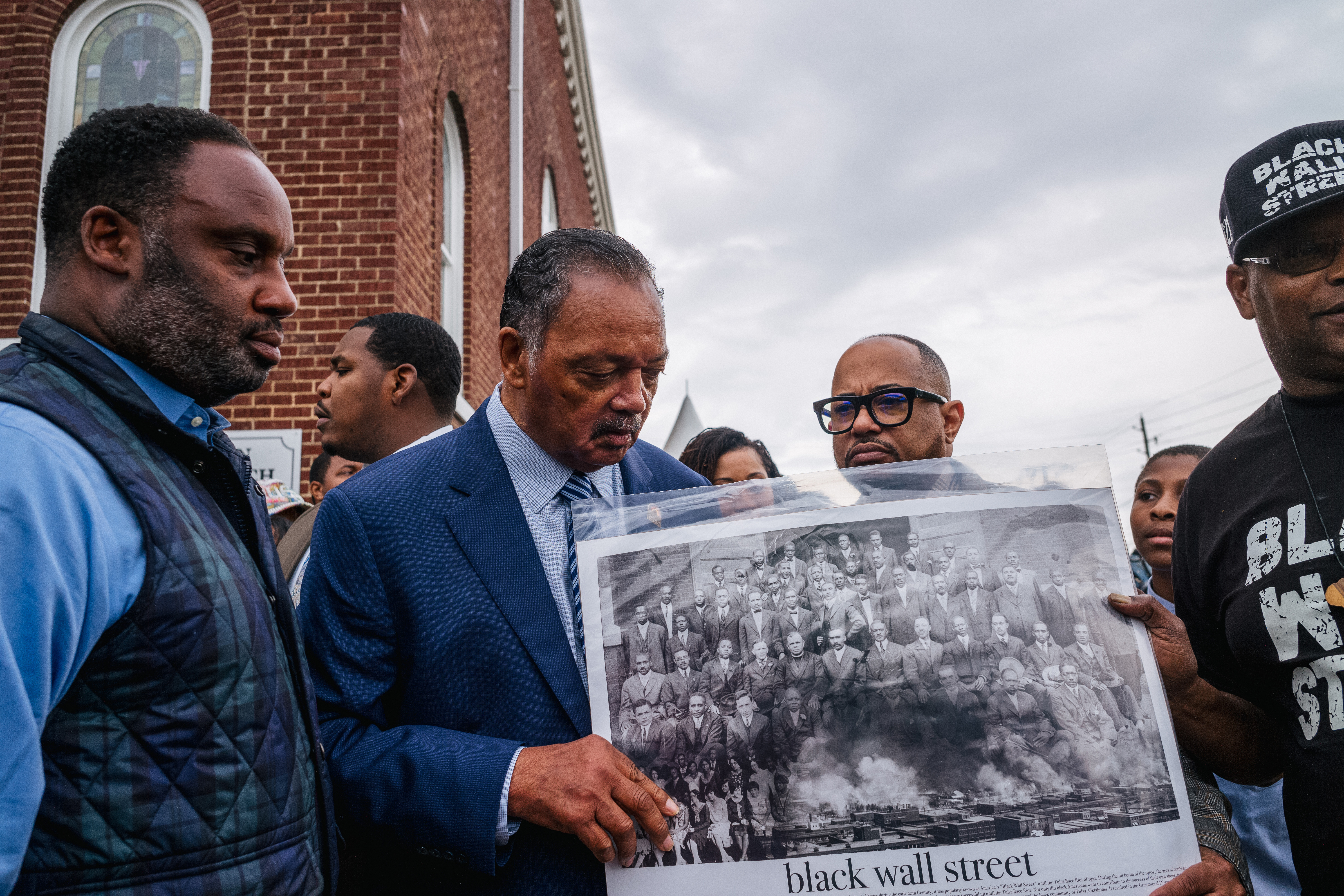 Rev. Jesse Jackson views a Black Wall Street poster board alongside community residents during a Prayer Wall memorial gathering.