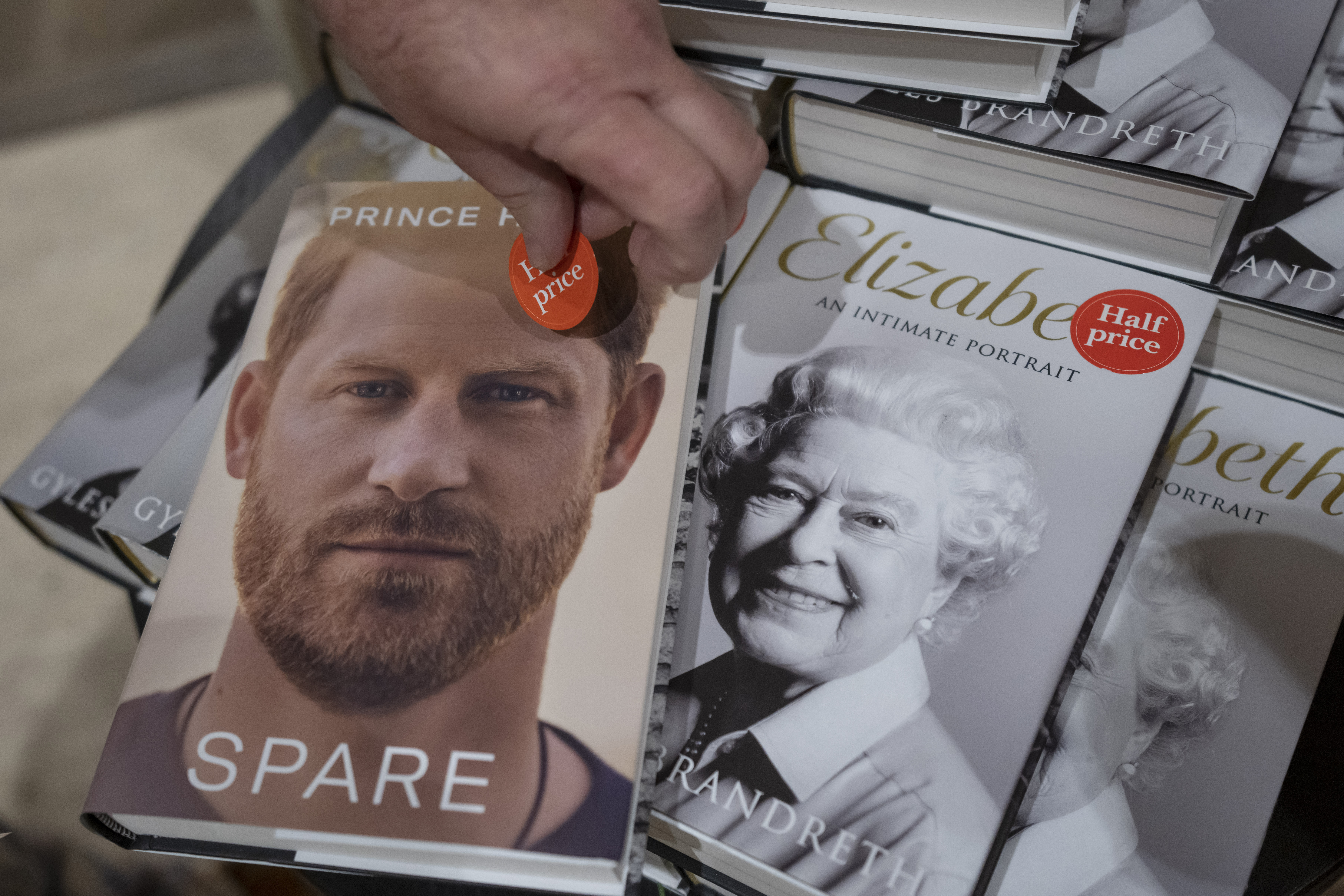 A member of staff places a half price sticker on copies of the new book by Prince Harry called "Spare" next to the copies of book featuring Queen Elizabeth II at a book store in London, Tuesday, Jan. 10, 2023. 