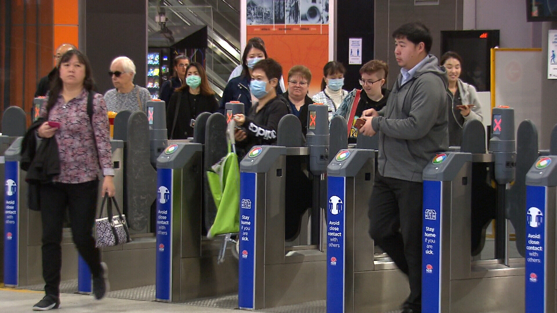 Sydney commuters at Chatswood train station in May, some wearing face masks, make their way to the platform to try and board a train.