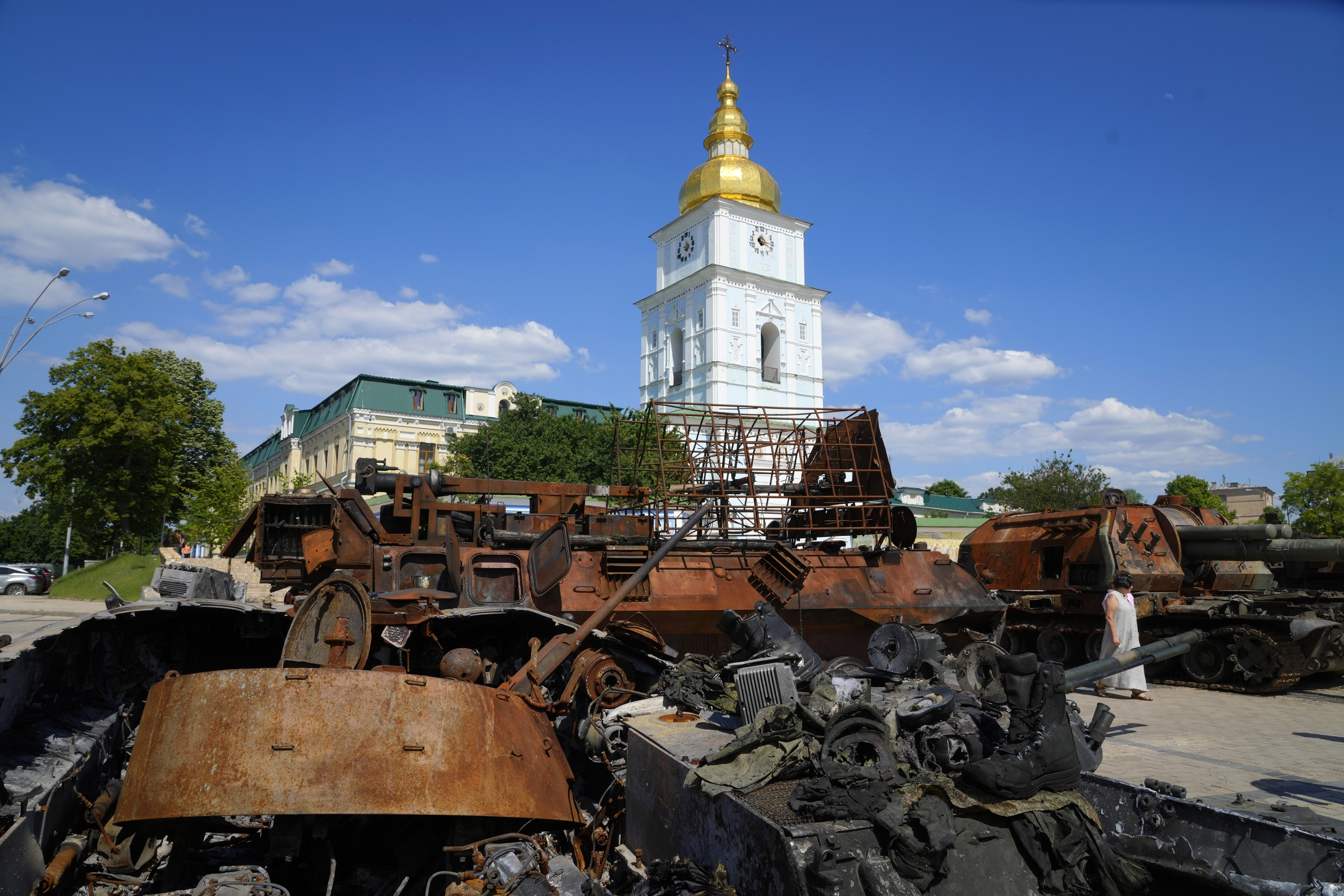 A woman looks at a destroyed Russian tanks installed as a symbol of war in central Kyiv, Ukraine, Tuesday, June 7, 2022. St Michael cathedral is in the background.