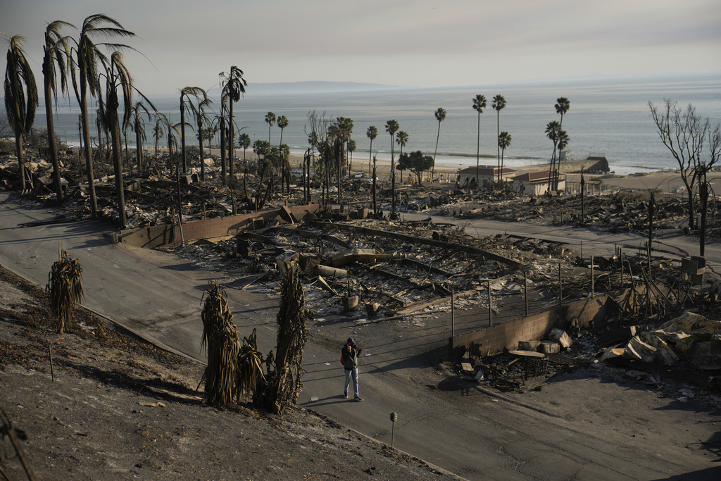 A person walks past damage from the Palisades Fire on Friday, Jan. 10, 2025, in the Pacific Palisades section of Los Angeles. (AP Photo/John Locher)