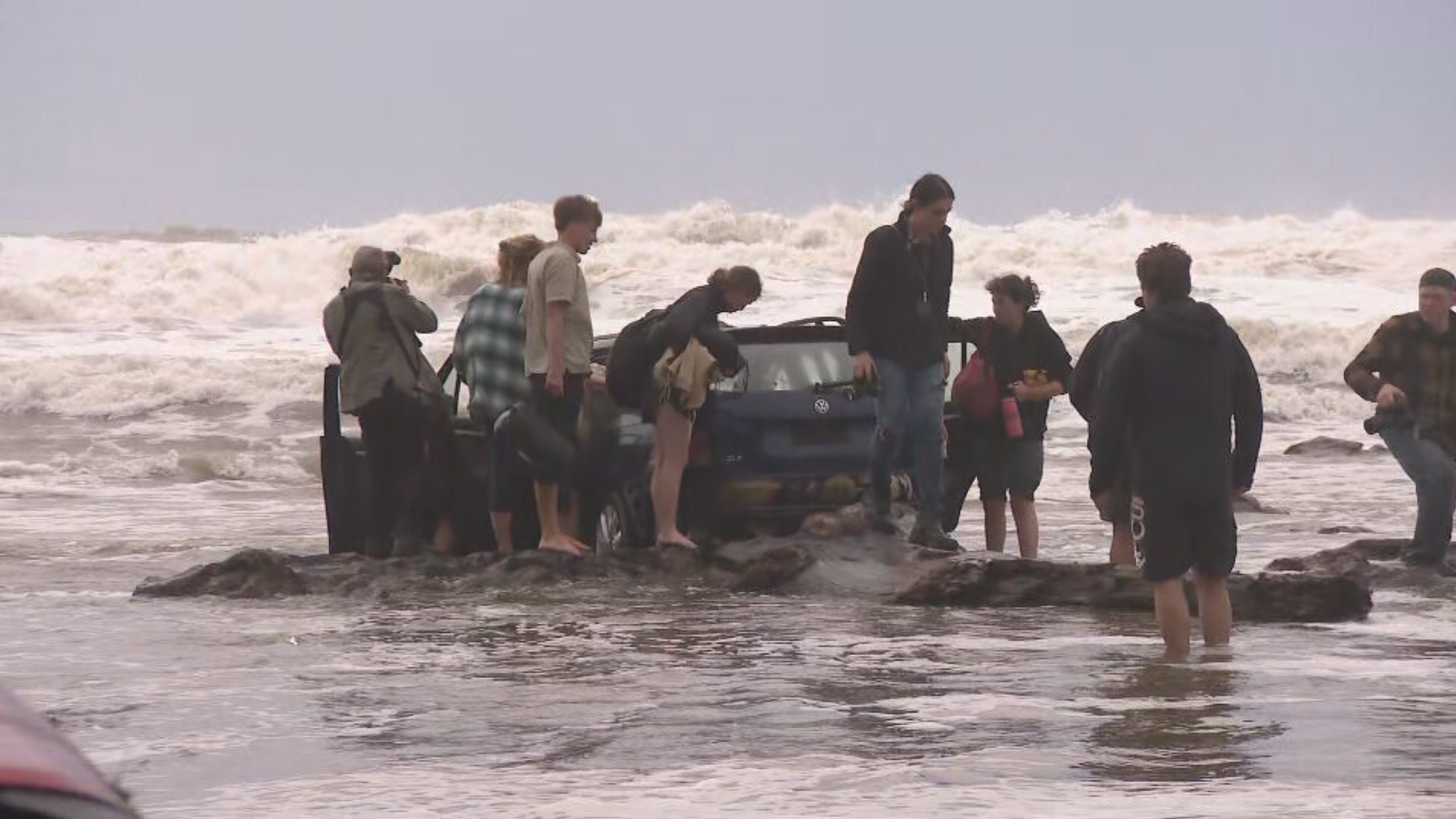 Campers salvage their belongings from a car that washed up on the beach after yesterday's flood.