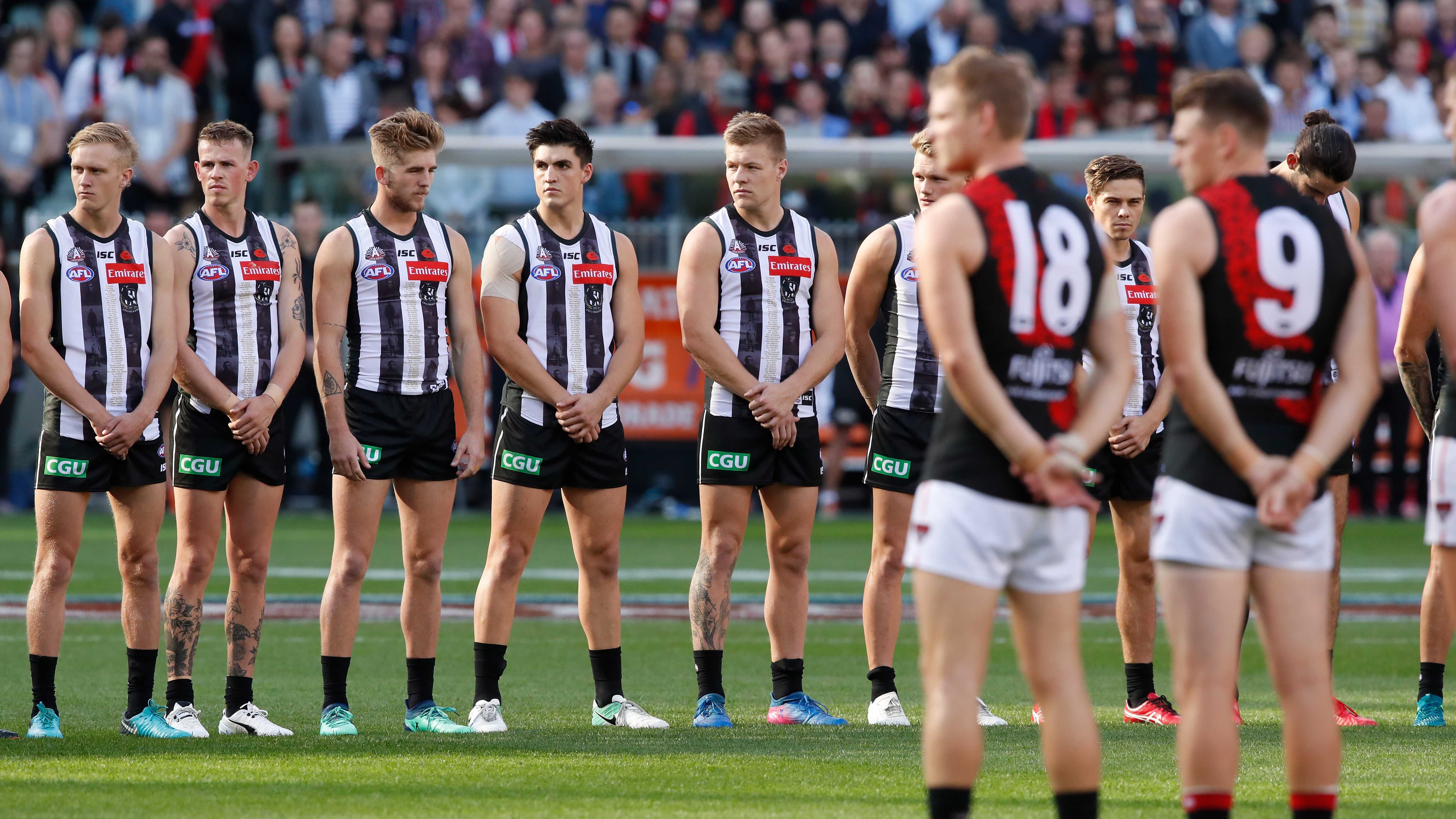 Collingwood and Essendon players line up at the start of an Anzac Day match.