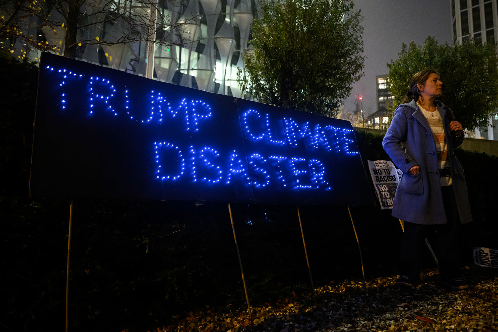 A woman stands beside a banner reading "Trump Climate Disaster" as a small group of demonstrators hold a protest against the new Trump Presidency 