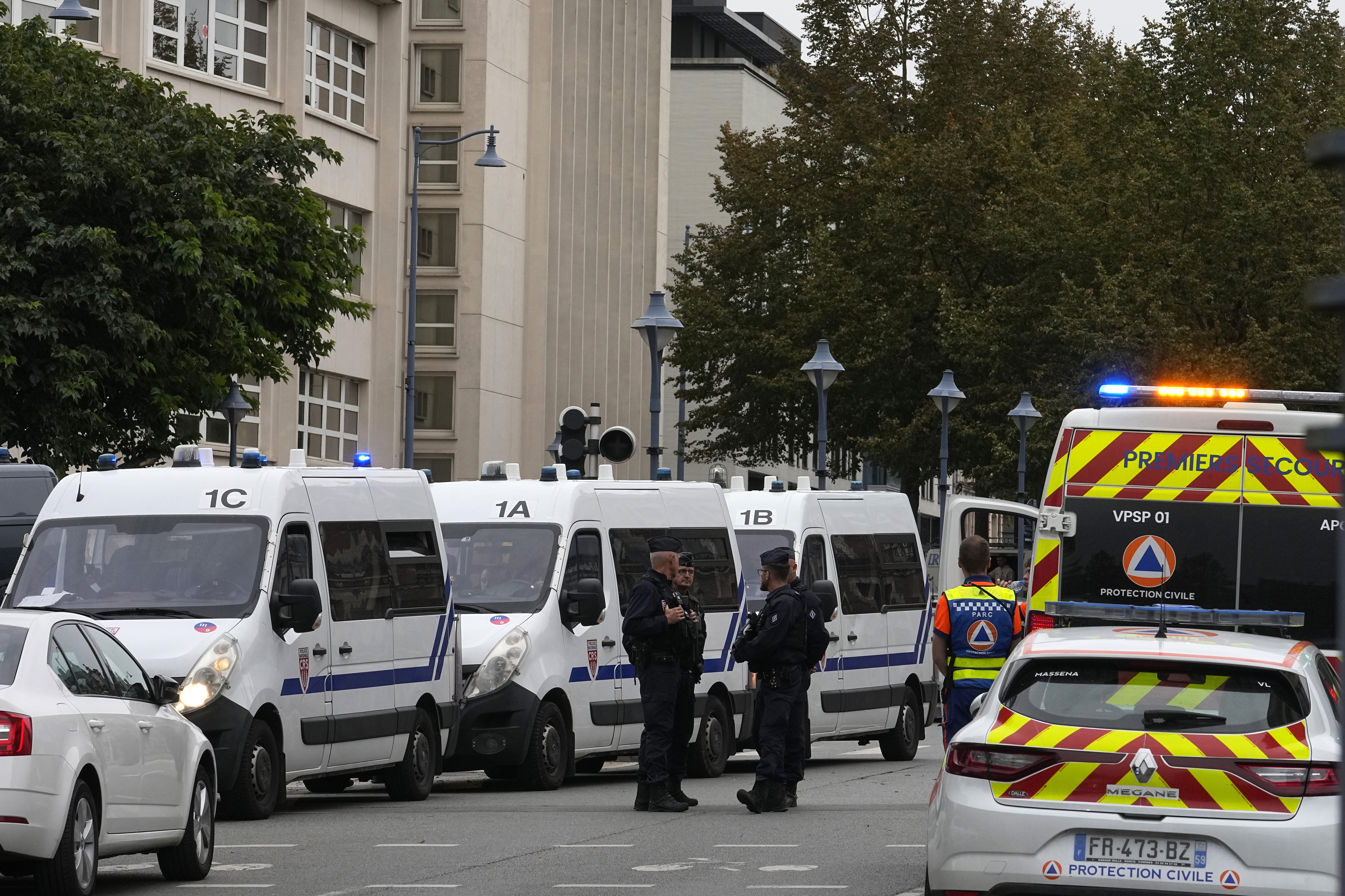 Police officers and rescue workers stand by the Gambetta high school after a man armed with a knife killed a teacher and wounded two others in Arras, northern France, Friday, Oct. 13, 2023.  
