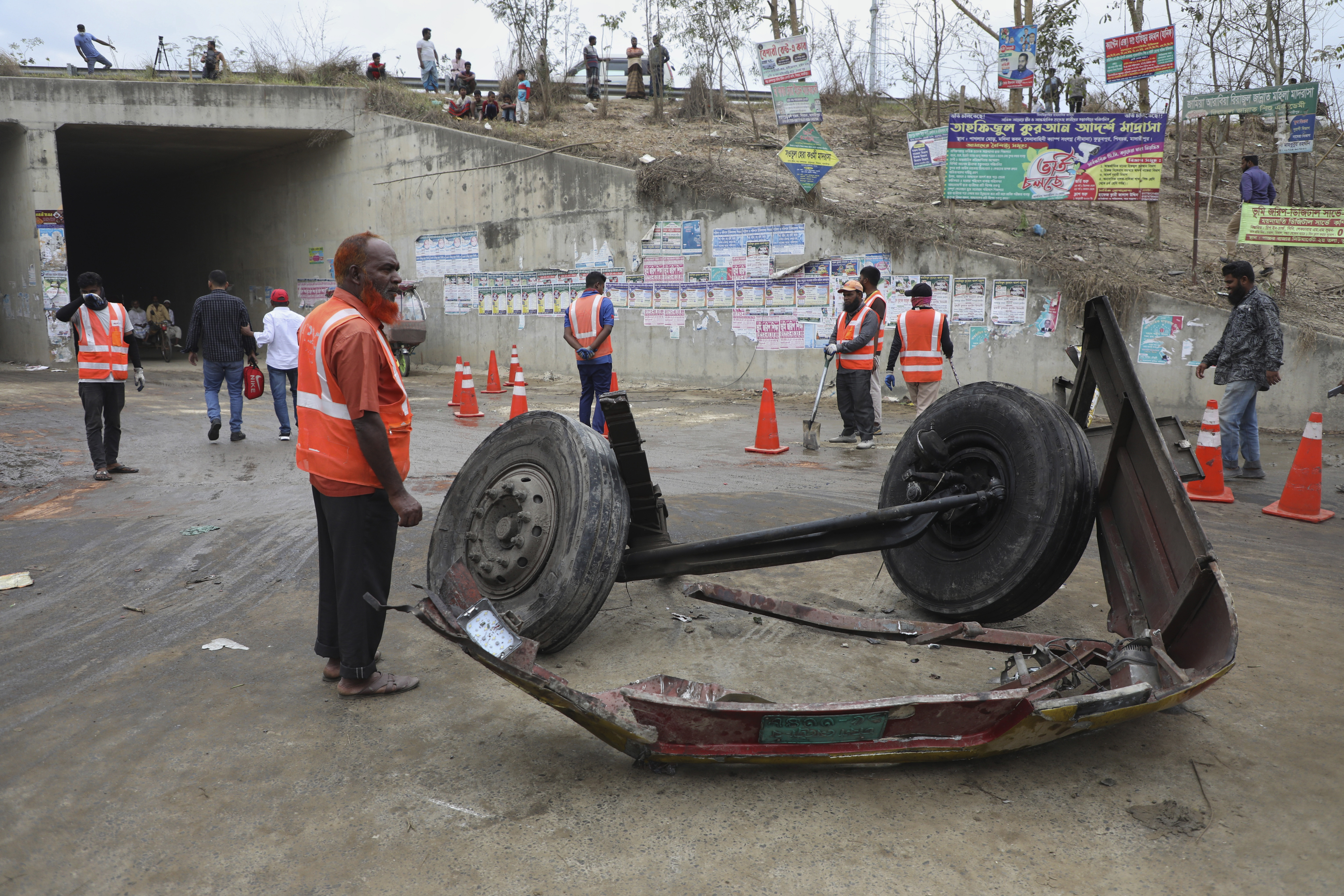Volunteers stand near the wreckage of a bus that fell into a roadside ditch in Shibchar area in Madaripur district, Bangladesh, Sunday, March 19, 2023.