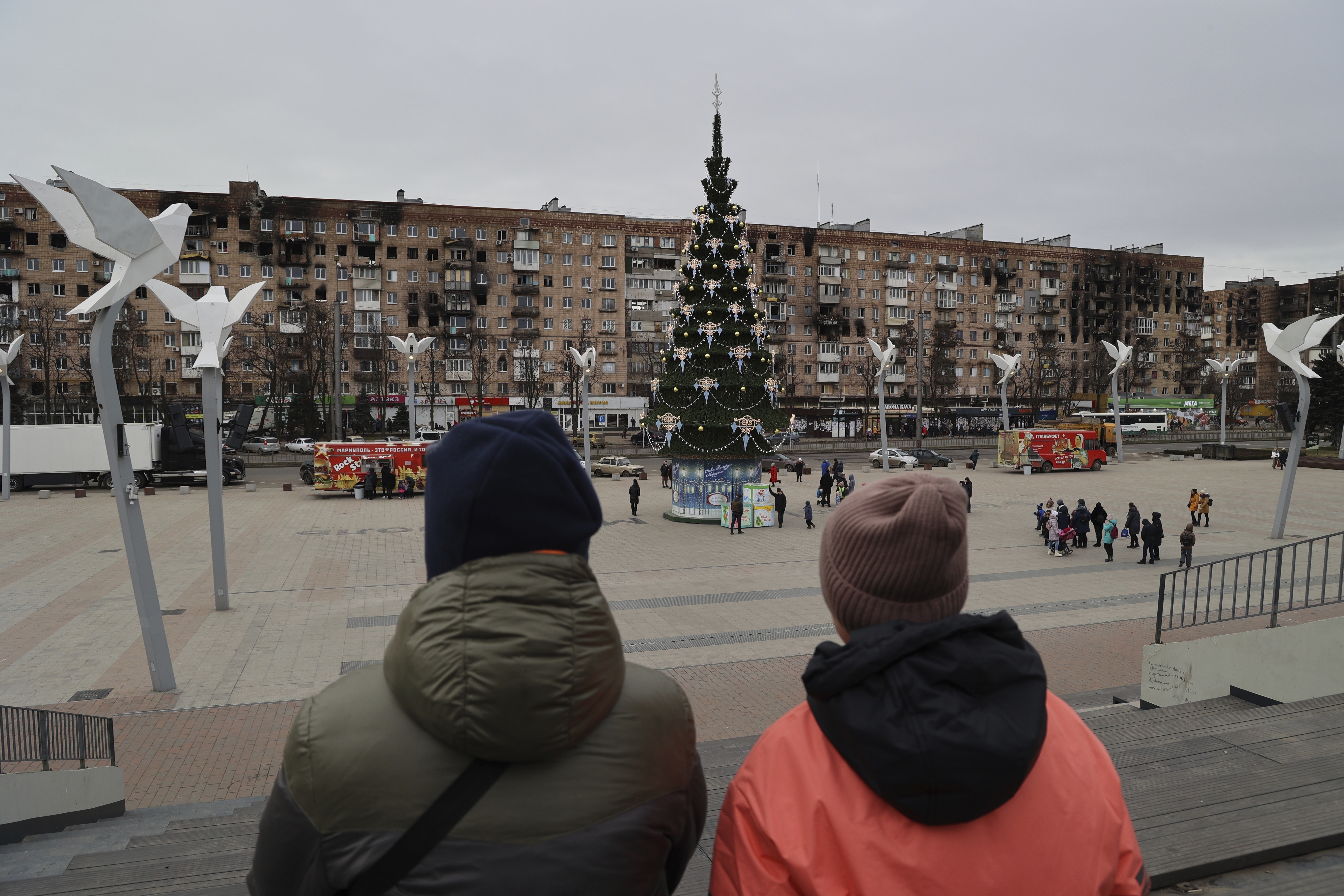 Local citizens walk near a Christmas tree decorated for Orthodox Christmas and the New Year festivities in Mariupol, in Russian-controlled Donetsk region, eastern Ukraine, Thursday, Jan. 5, 2023. (AP Photo/Alexei Alexandrov)