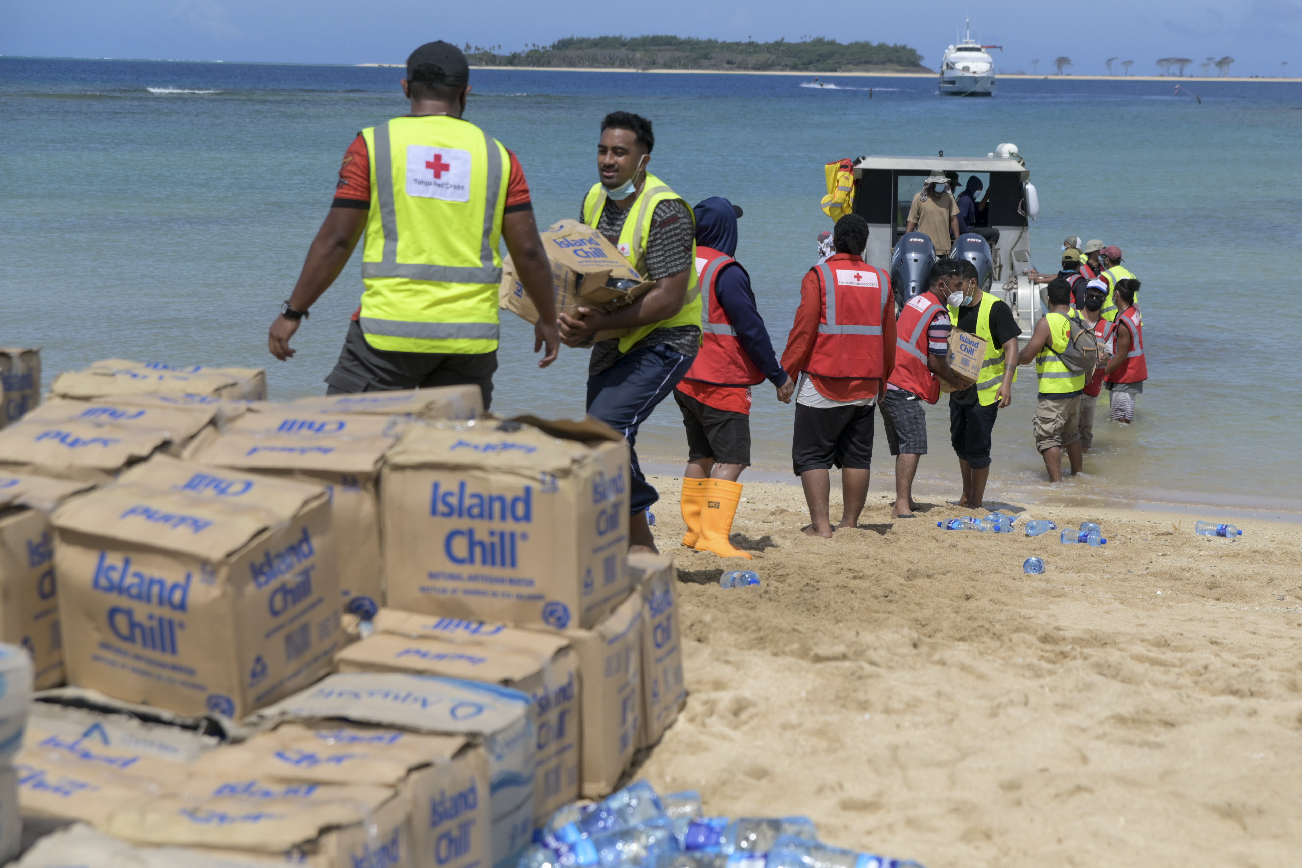 In this photo provided by Malau Media/IFRC, Tonga Red Cross Society's staff and volunteers unloading boxes of water bottles from the boat into the beach in Nomuka Ha'apai Island, Tonga on April 1, 2022. Three months on from a devastating volcano and tsunami in Tonga, the AP checks in on how the island nation is recovering. The bill from the tsunami is estimated at some $90 million and GDP is expected to fall by more than 7% this year. The cleanup has been hindered by an internet outage caused by