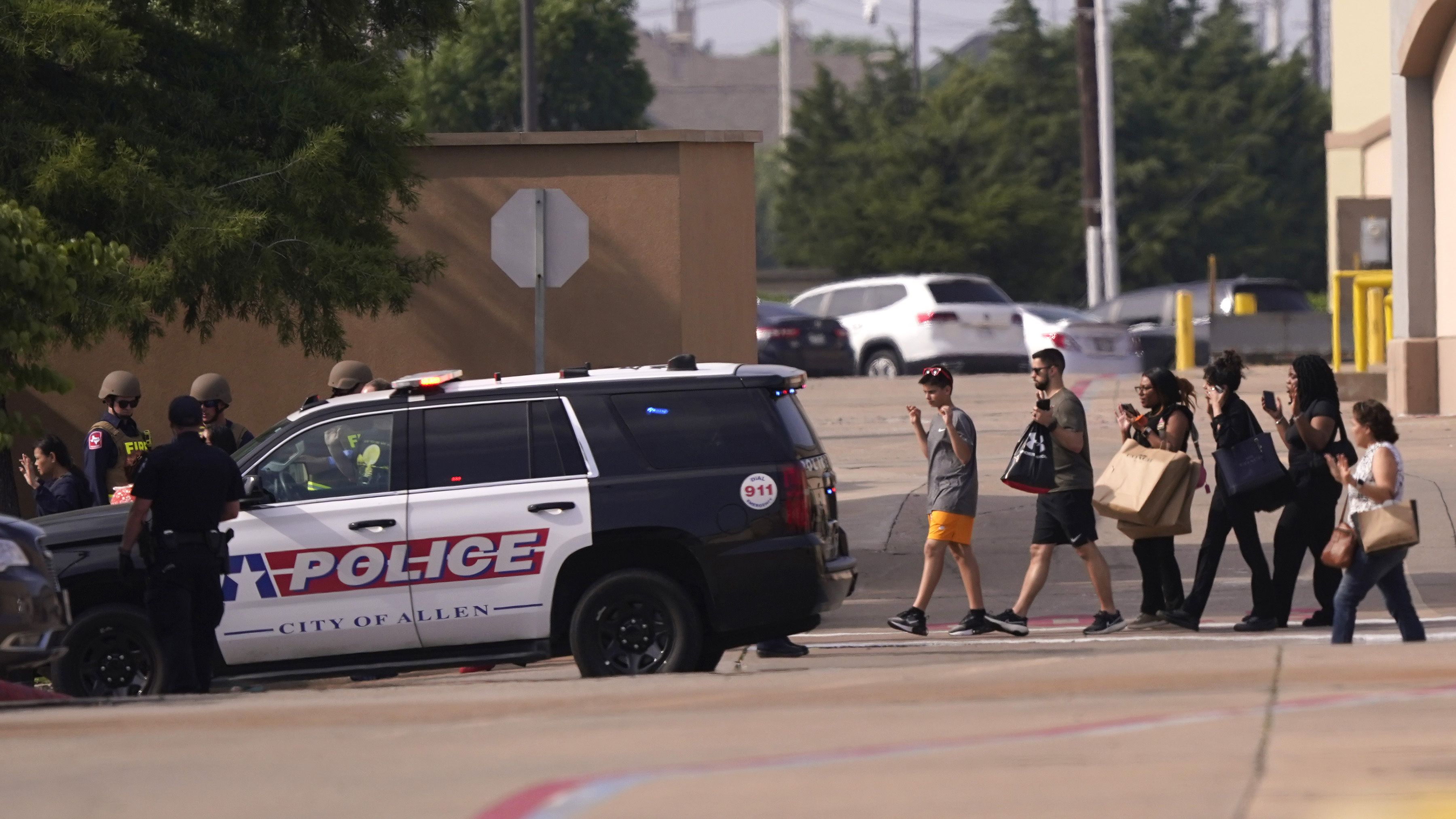 People raise their hands as they leave a shopping centre after a shooting, Saturday, May 6, 2023, in Allen, Texas.