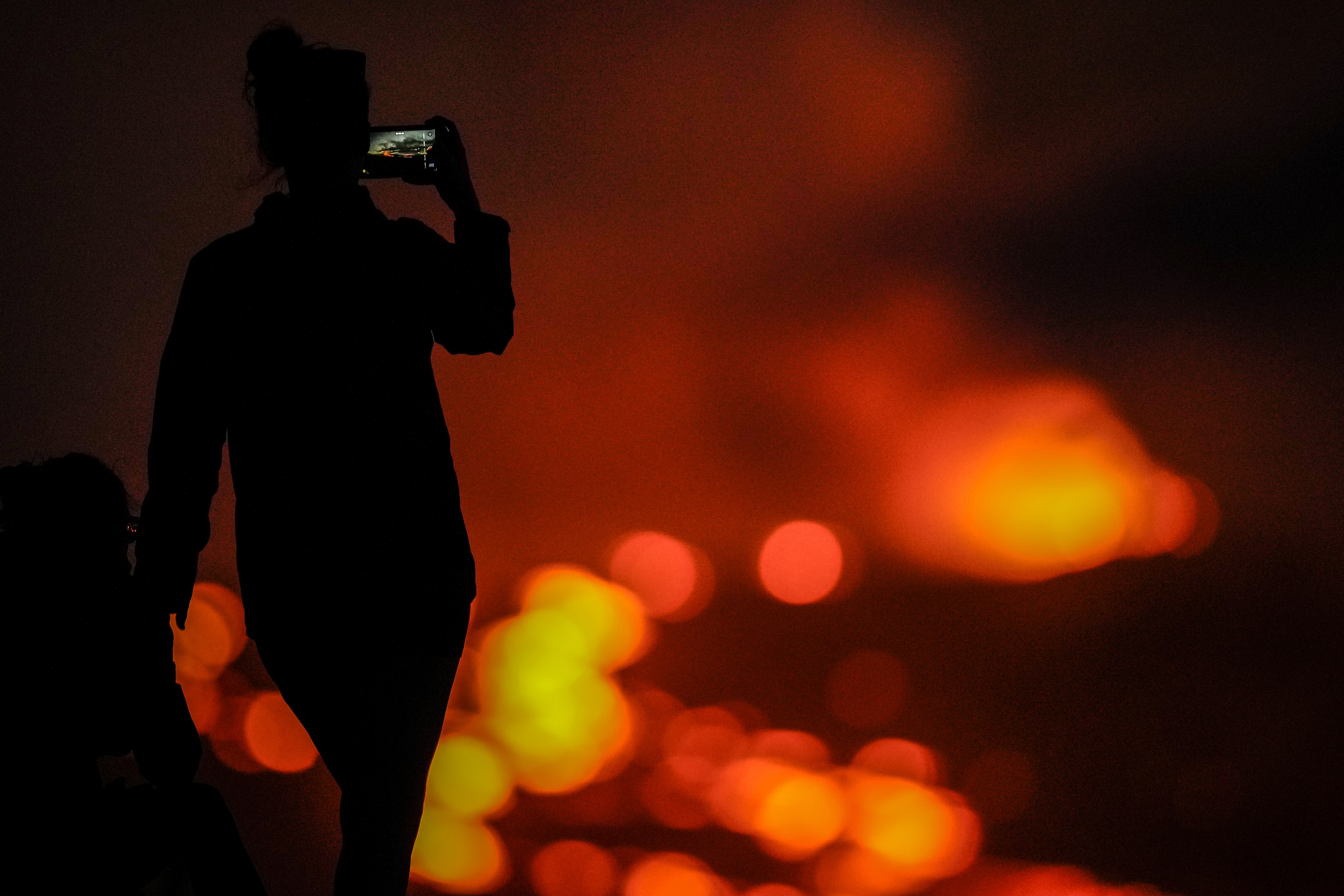A woman records with her phone as lava erupts from the Mauna Loa volcano Thursday, December 1, 2022, near Hilo, Hawaii. 