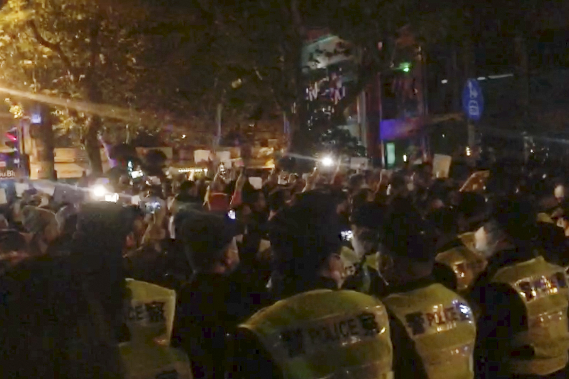 In this image from video obtained by The Associated Press, police, foreground, watch protesters in Shanghai on Saturday, Nov. 26, 2022. Protests against Chinas restrictive COVID measures appeared in a number of cities Saturday night, in displays of public defiance fanned by anger over a deadly fire in the western Xinjiang region.